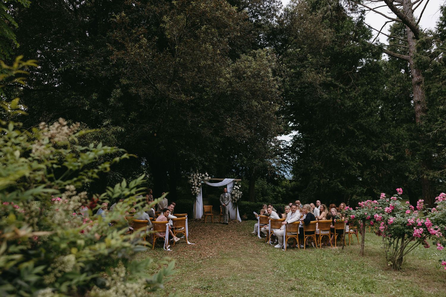 An outdoor wedding ceremony setup with wooden chairs arranged in rows among trees and natural scenery.