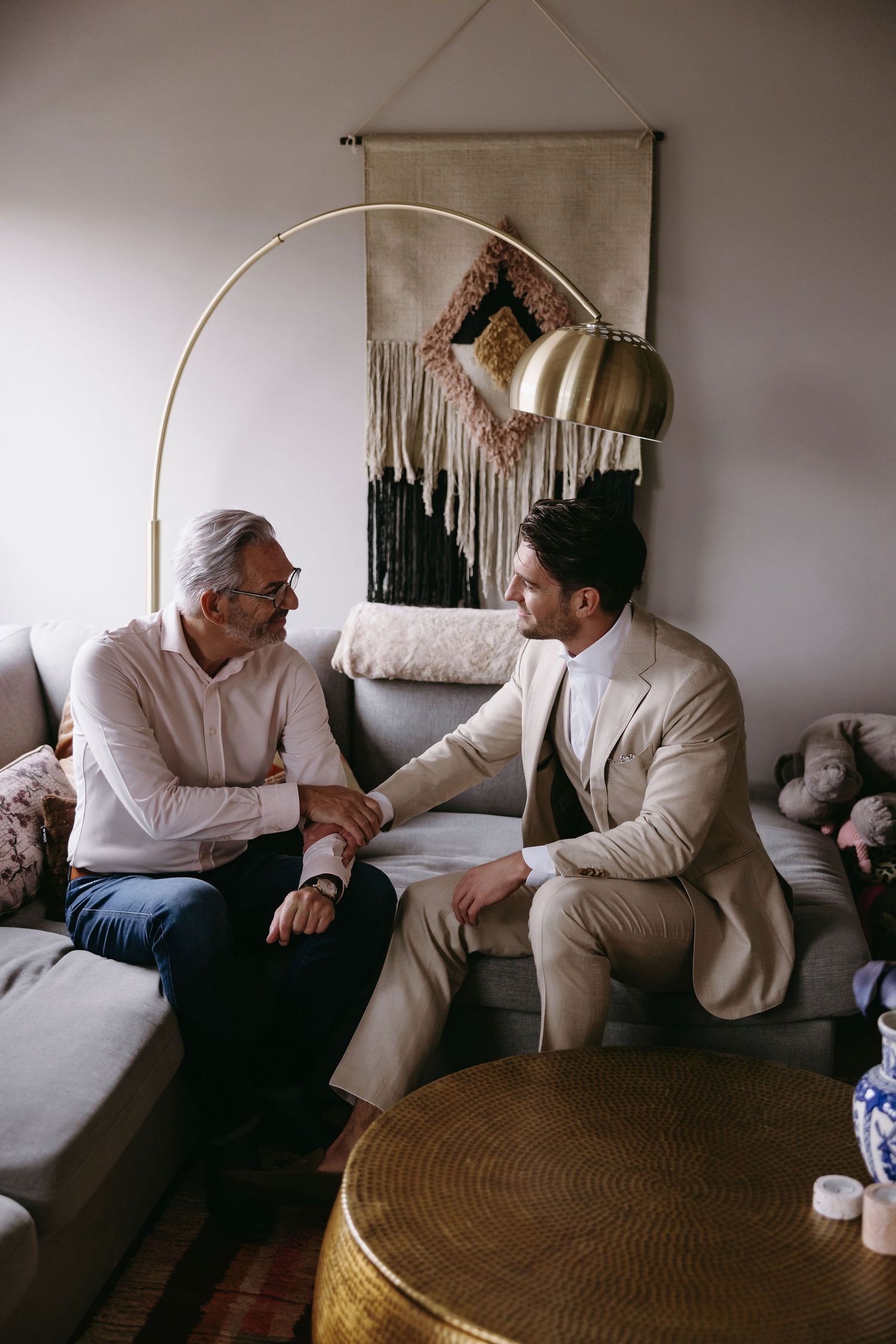 Two people in light colored clothing having conversation on grey couch.