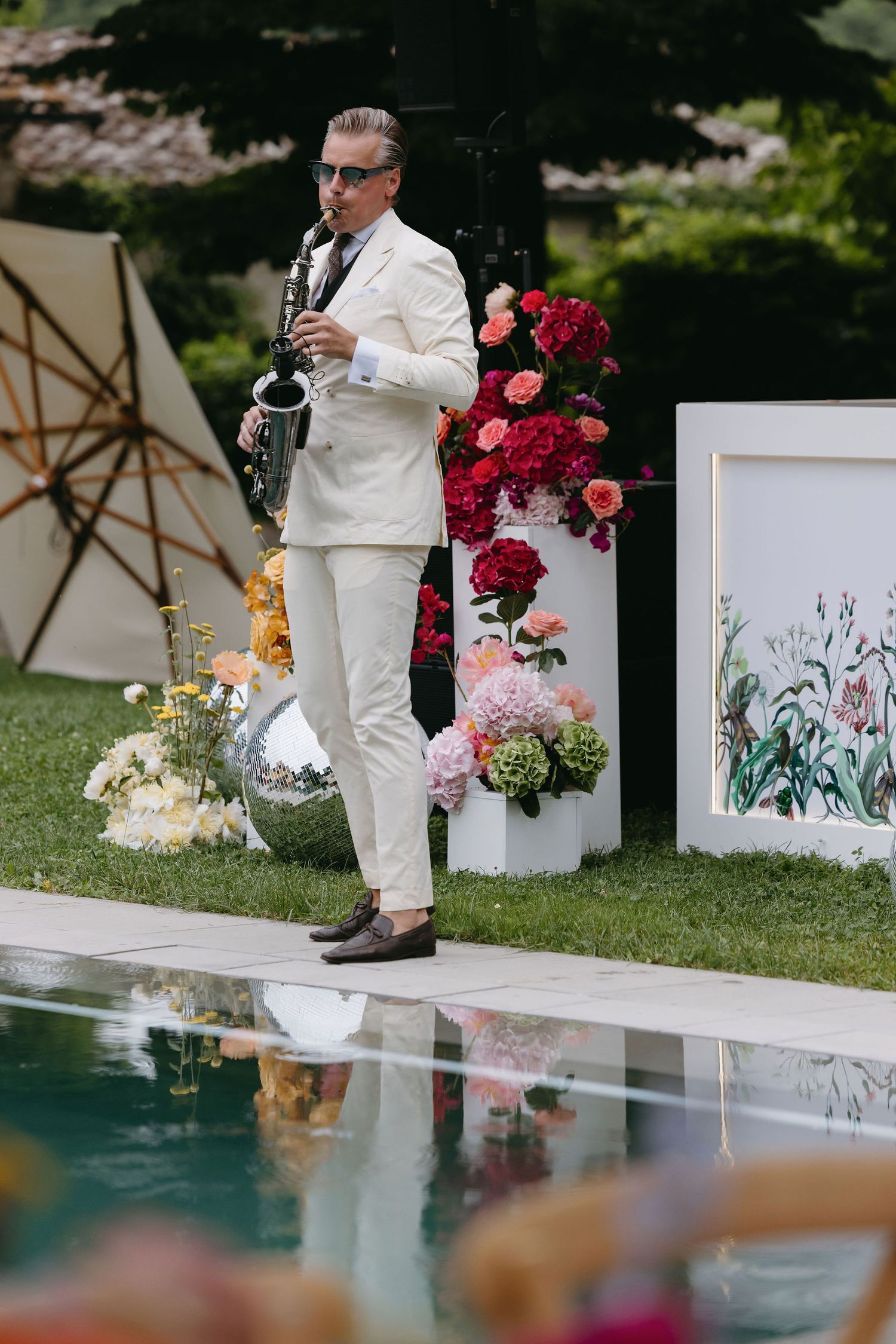 Elegant wedding decor with white floral panels and red roses arranged along a poolside setting.
