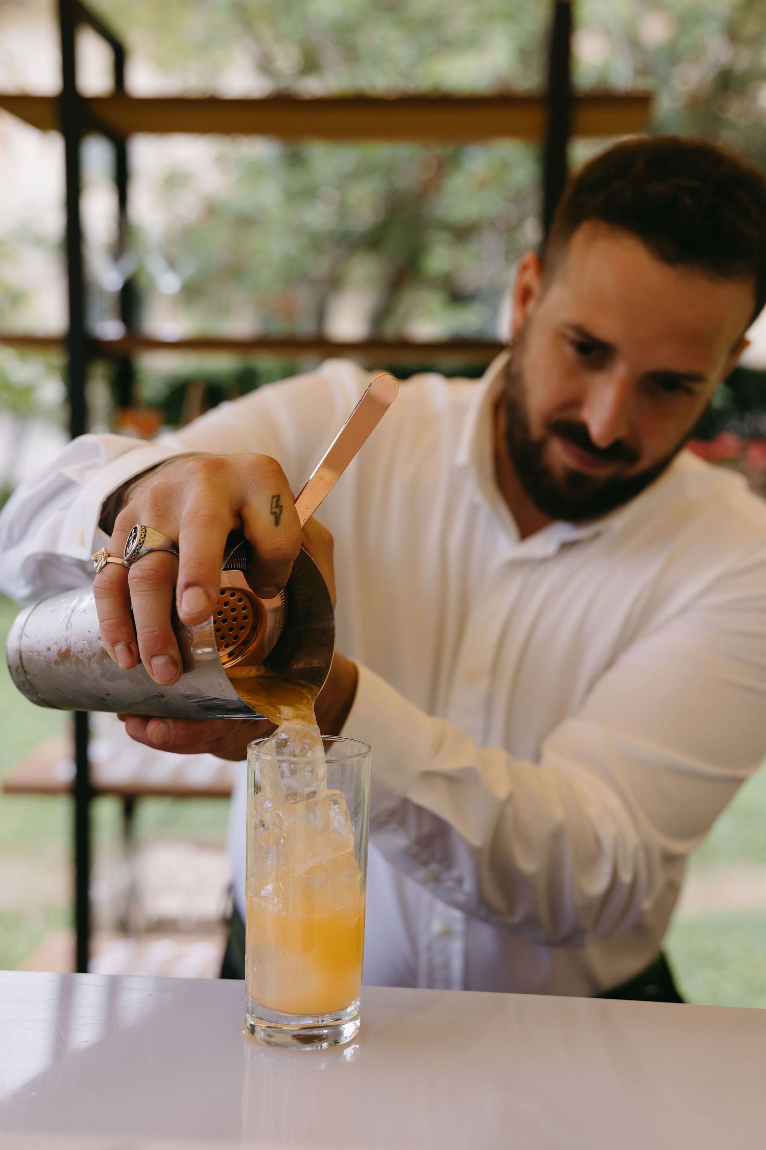 Bartender pouring a craft cocktail into a tall glass at an outdoor event.
