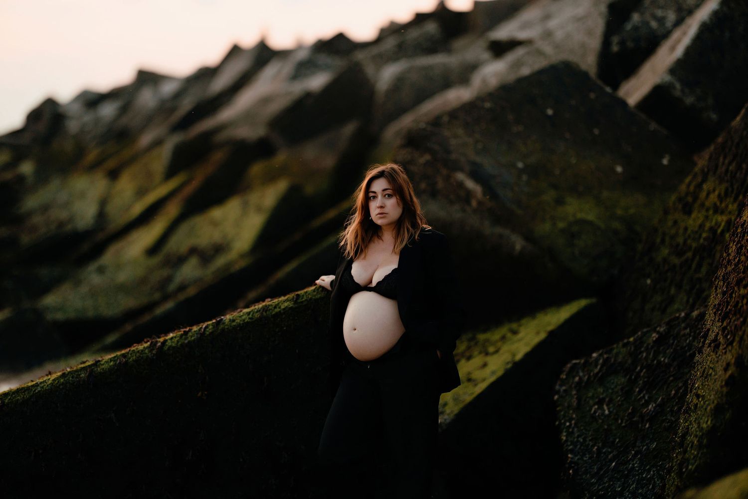 Dramatic maternity silhouette against rocky mountain landscape at sunset.