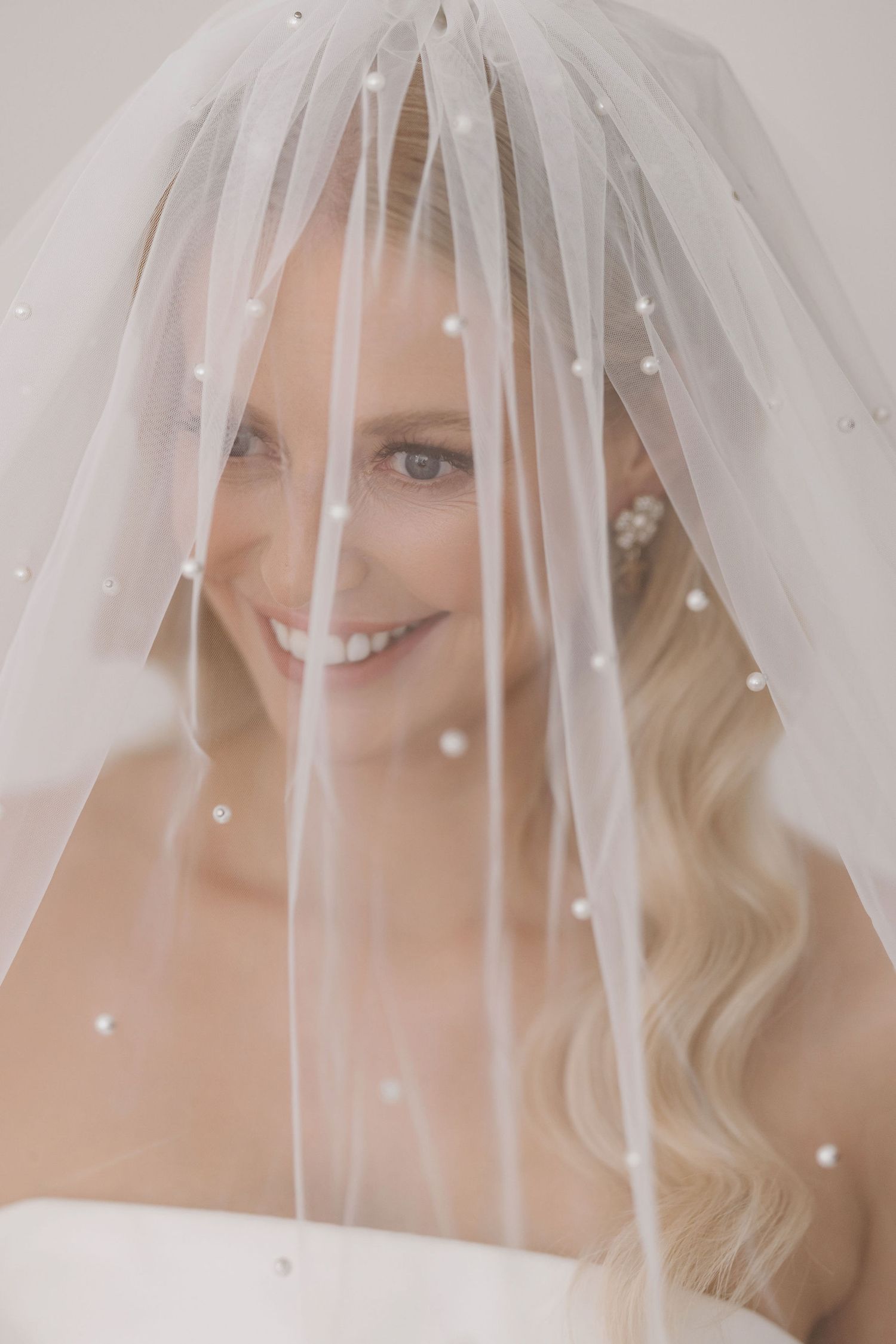 Elegant bridal portrait showing delicate pearl-detailed veil and soft natural makeup.