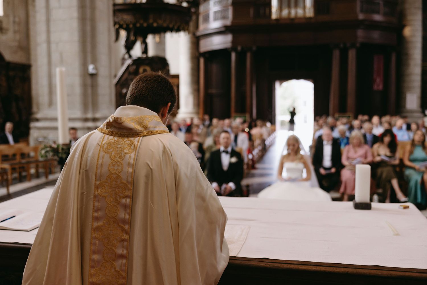 A priest leads a wedding ceremony in a grand cathedral filled with guests.