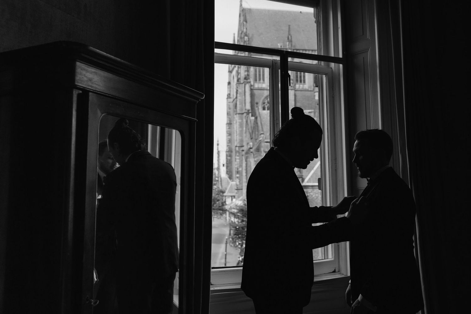 Silhouetted figures in dramatic lighting by window creating moody atmosphere.