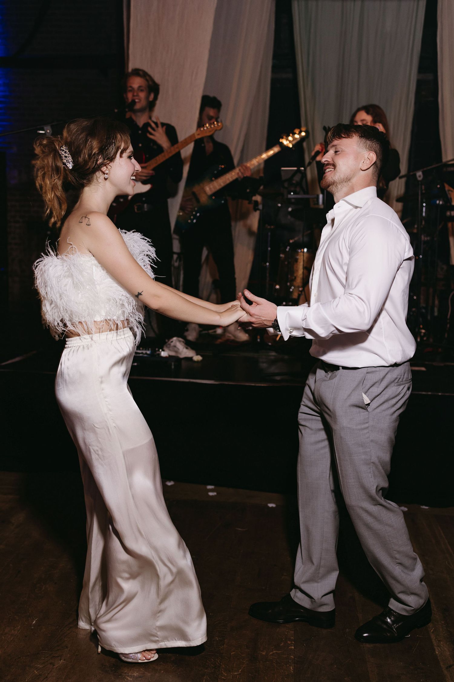 Couple dancing together at their wedding reception in formal attire with guests in the background.