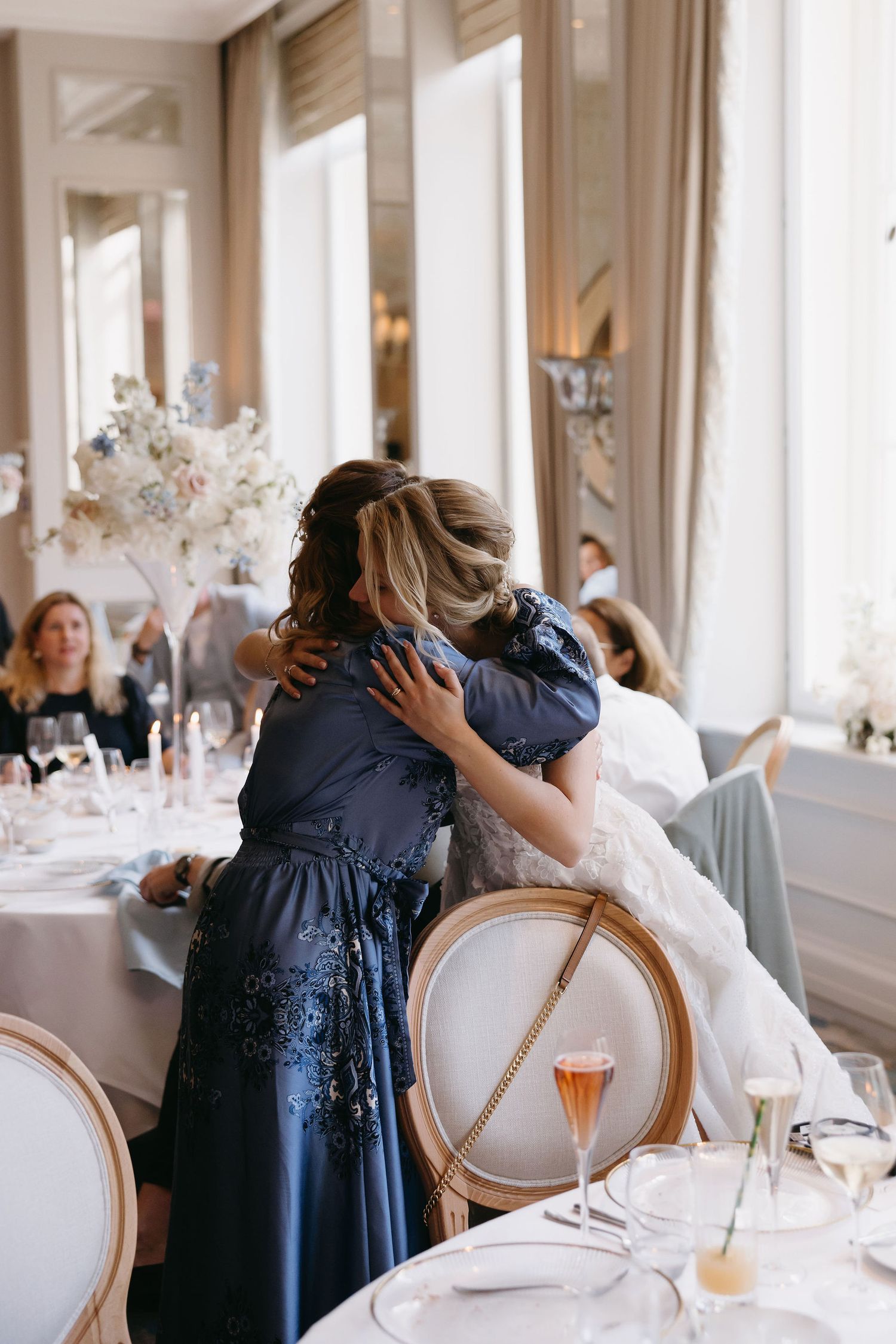 An emotional embrace captured during a wedding reception in an elegant dining room.