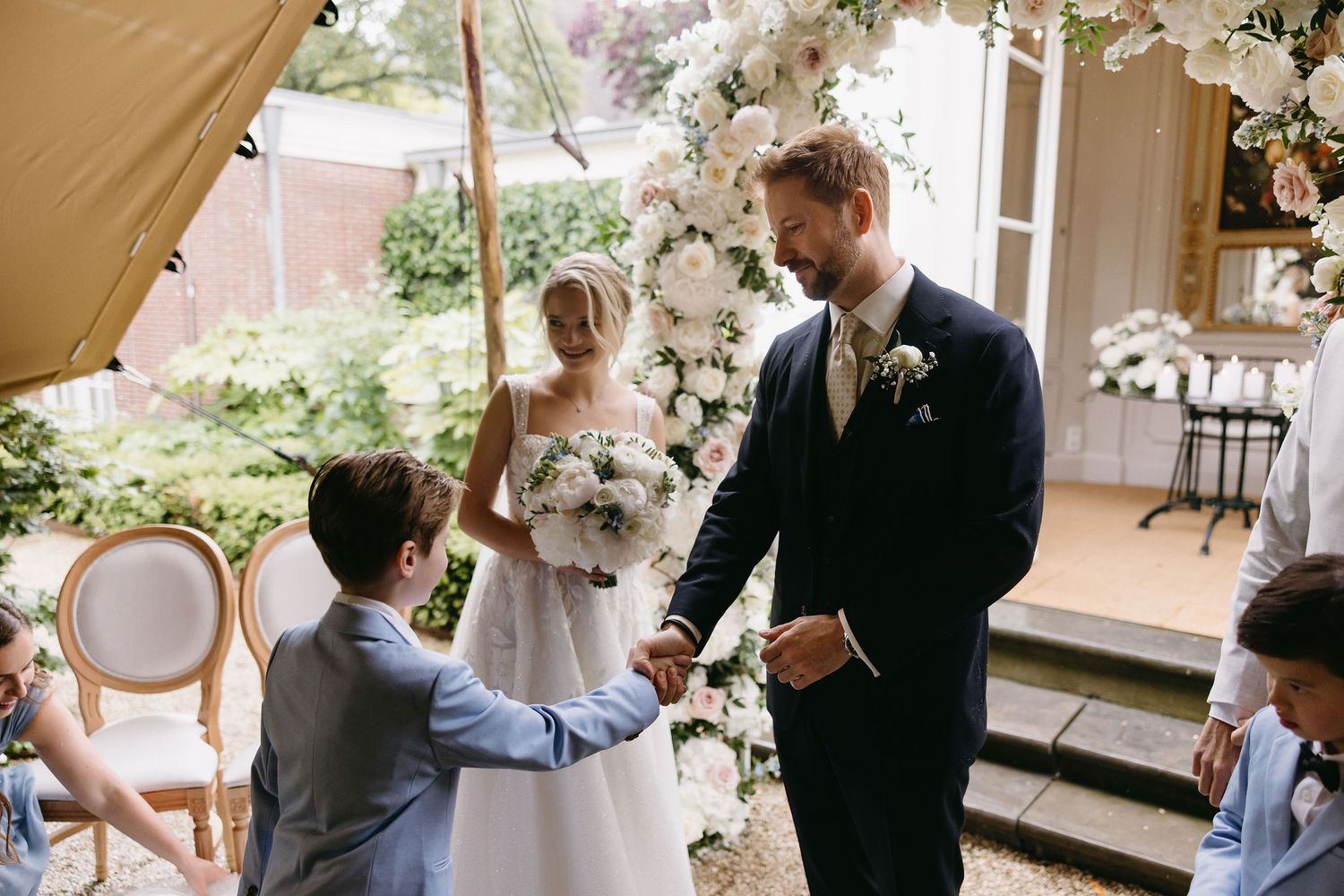 Wedding ceremony scene under a beige tent with floral decorations.
