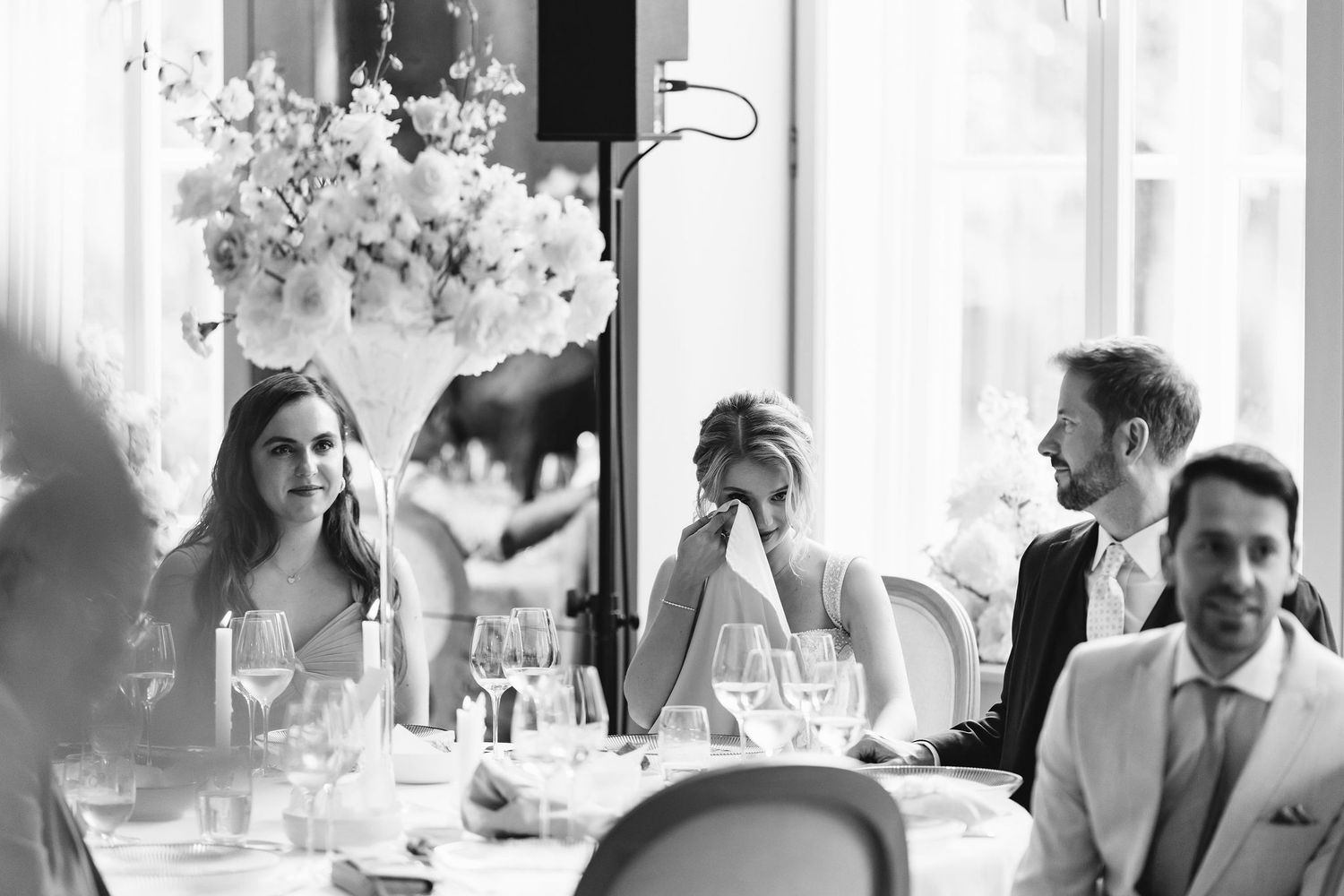 Elegant reception table setting with guests at a formal wedding dinner featuring floral centerpiece arrangements.