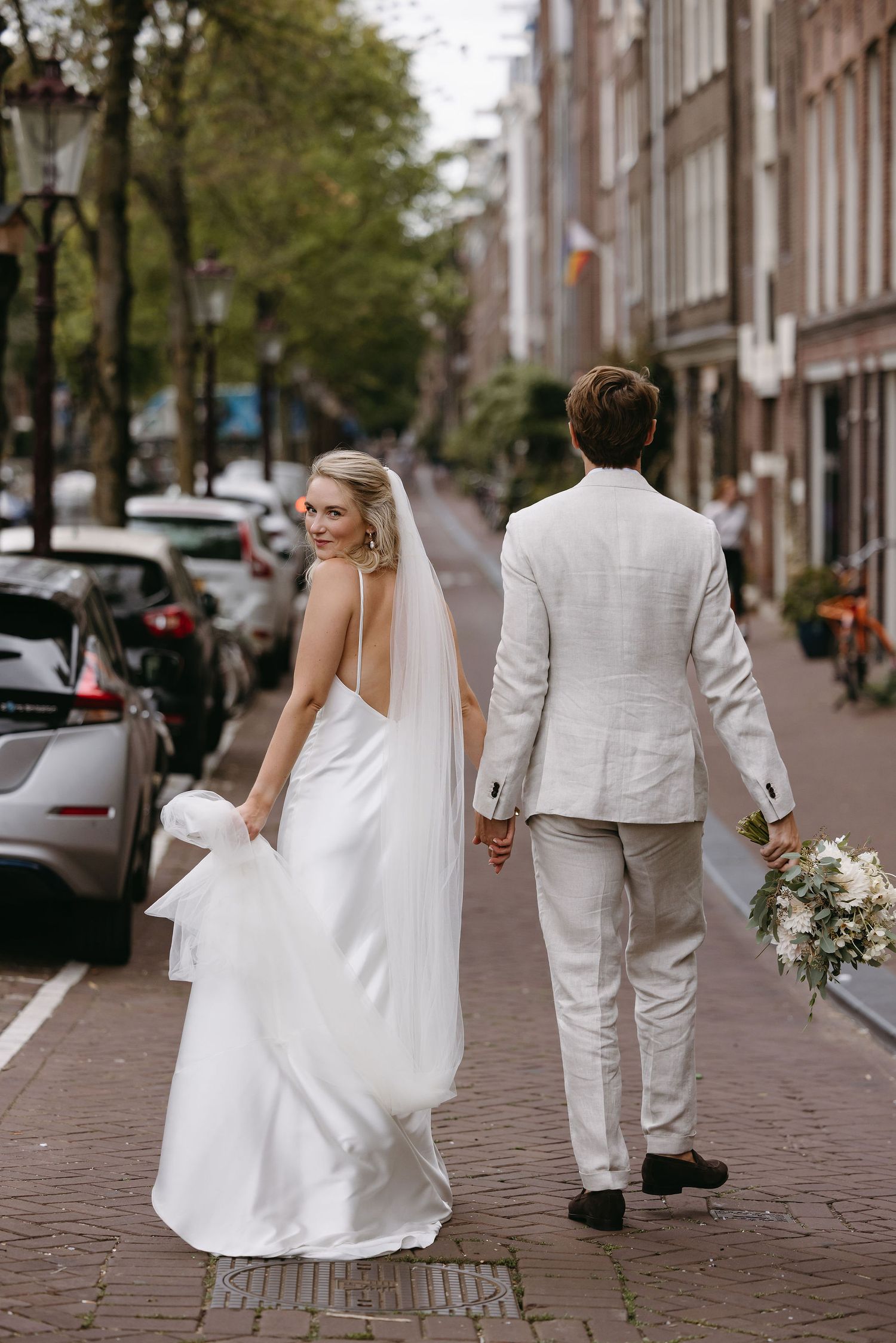 Bride and groom walking hand in hand on Amsterdam street.