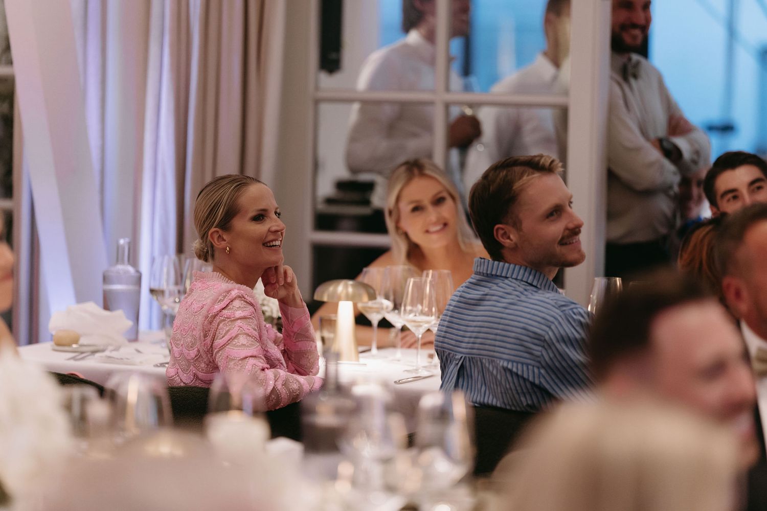 Wedding reception guests enjoy conversations at tables decorated with floral centerpieces.