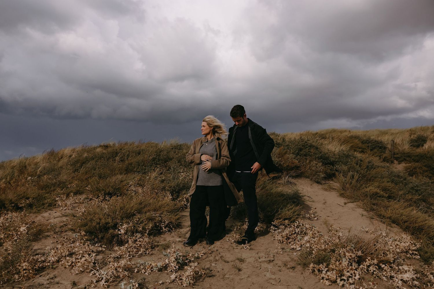 Couple enjoying a peaceful moment together on a hiking trail under cloudy skies.