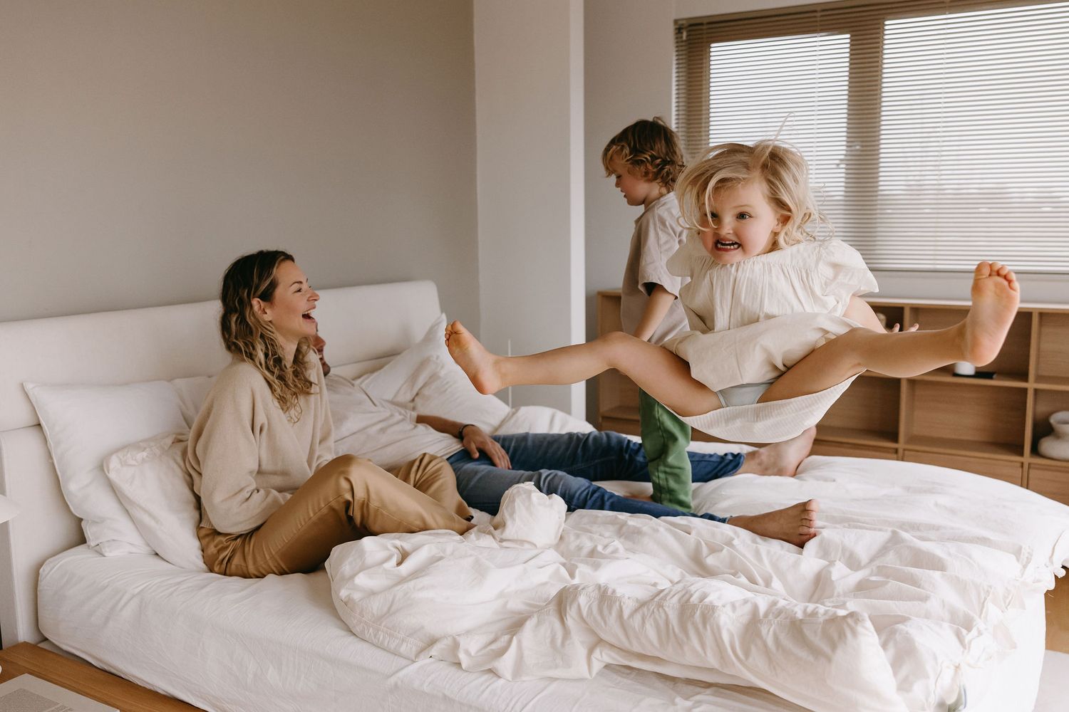 Lifestyle photos capture playful and tender moments in a bright, airy bedroom.