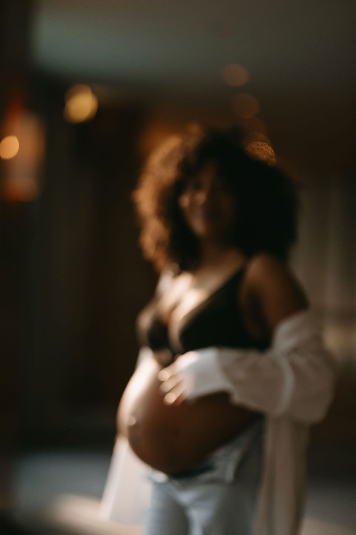 Artistic maternity silhouette with bokeh lighting effects and white clothing.