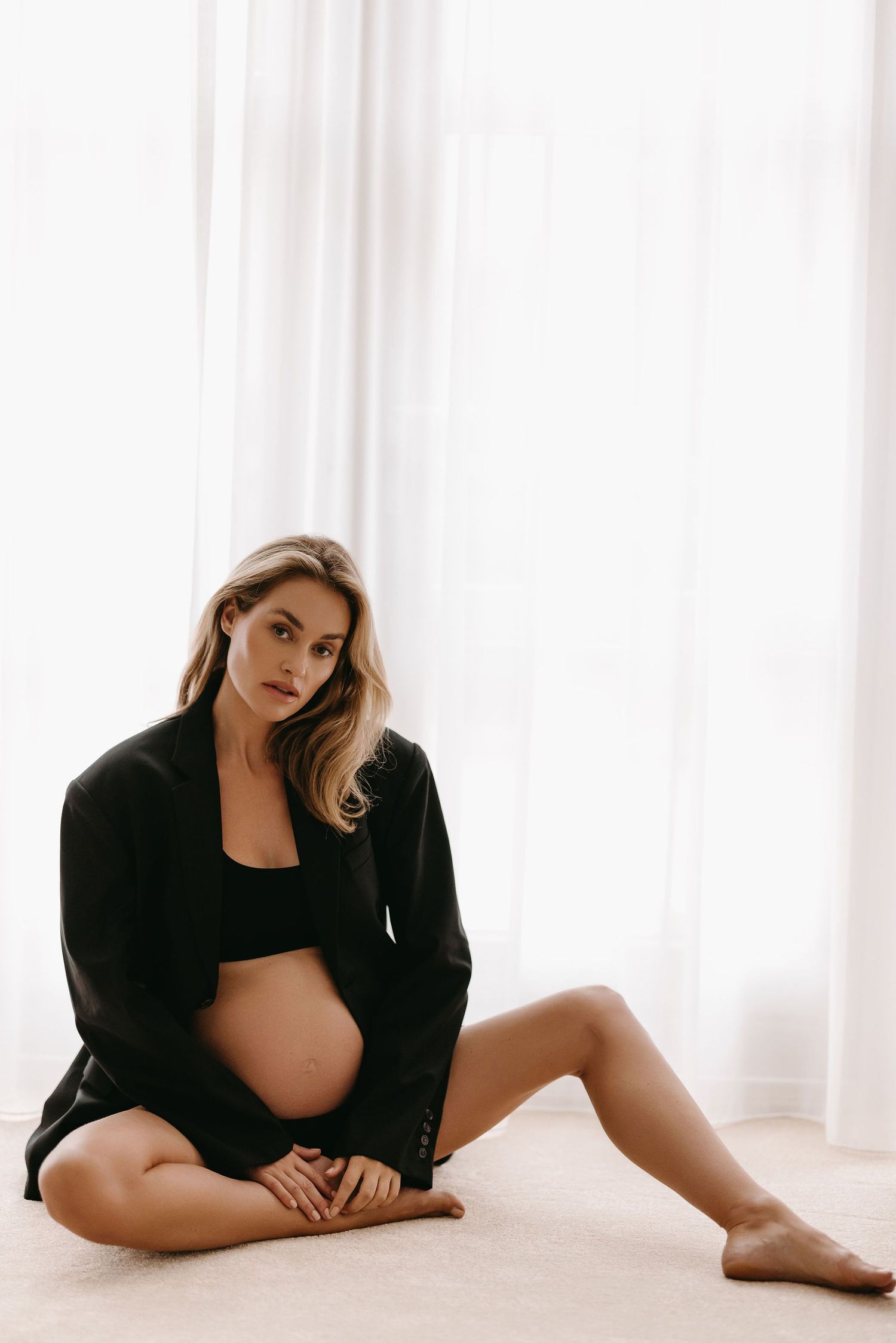 Minimalist maternity portrait against white curtains in black outfit.