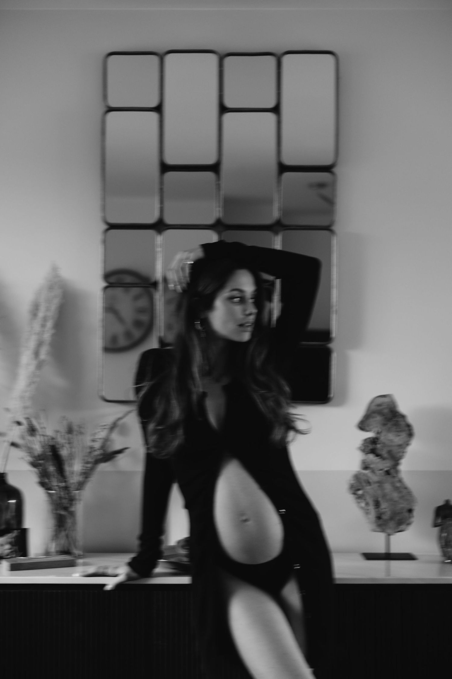 An artistic black and white photo of a woman in a cutout dress posing by geometric wall art.