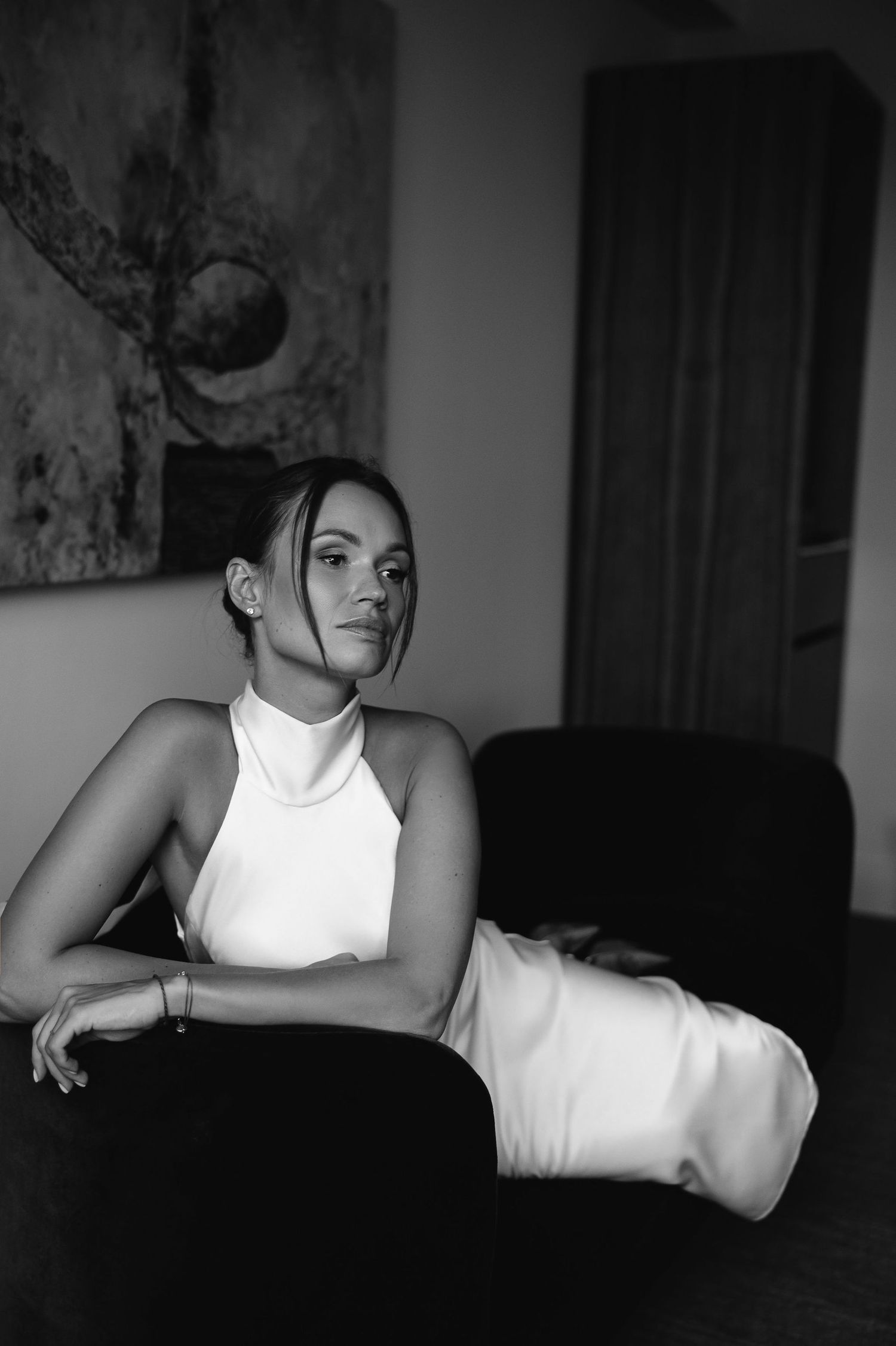 Black and white photograph of someone in an elegant white halter dress reclining on a dark couch.