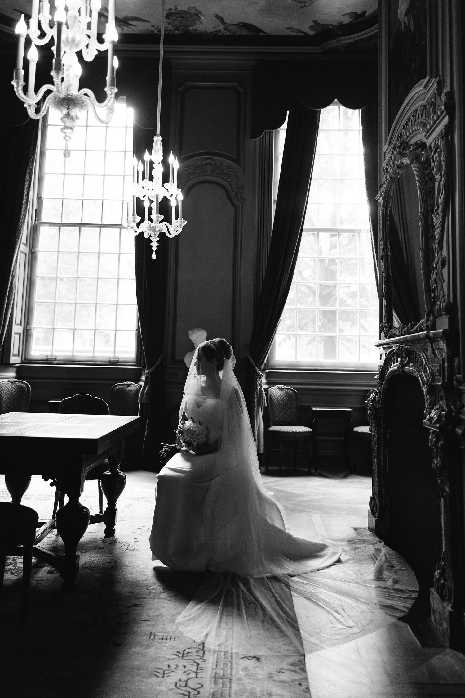 Wedding dress silhouettes cast dramatic shadows in an elegant ballroom with crystal chandeliers and ornate windows.