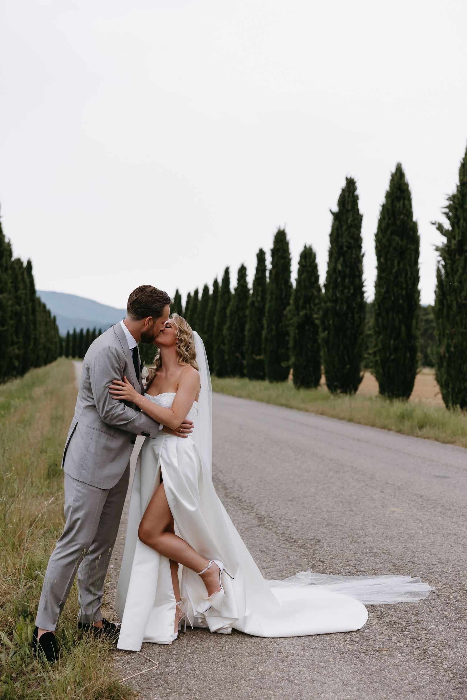 A romantic couple on a cypress-lined path in Italy captures a tender dip pose against a scenic backdrop.