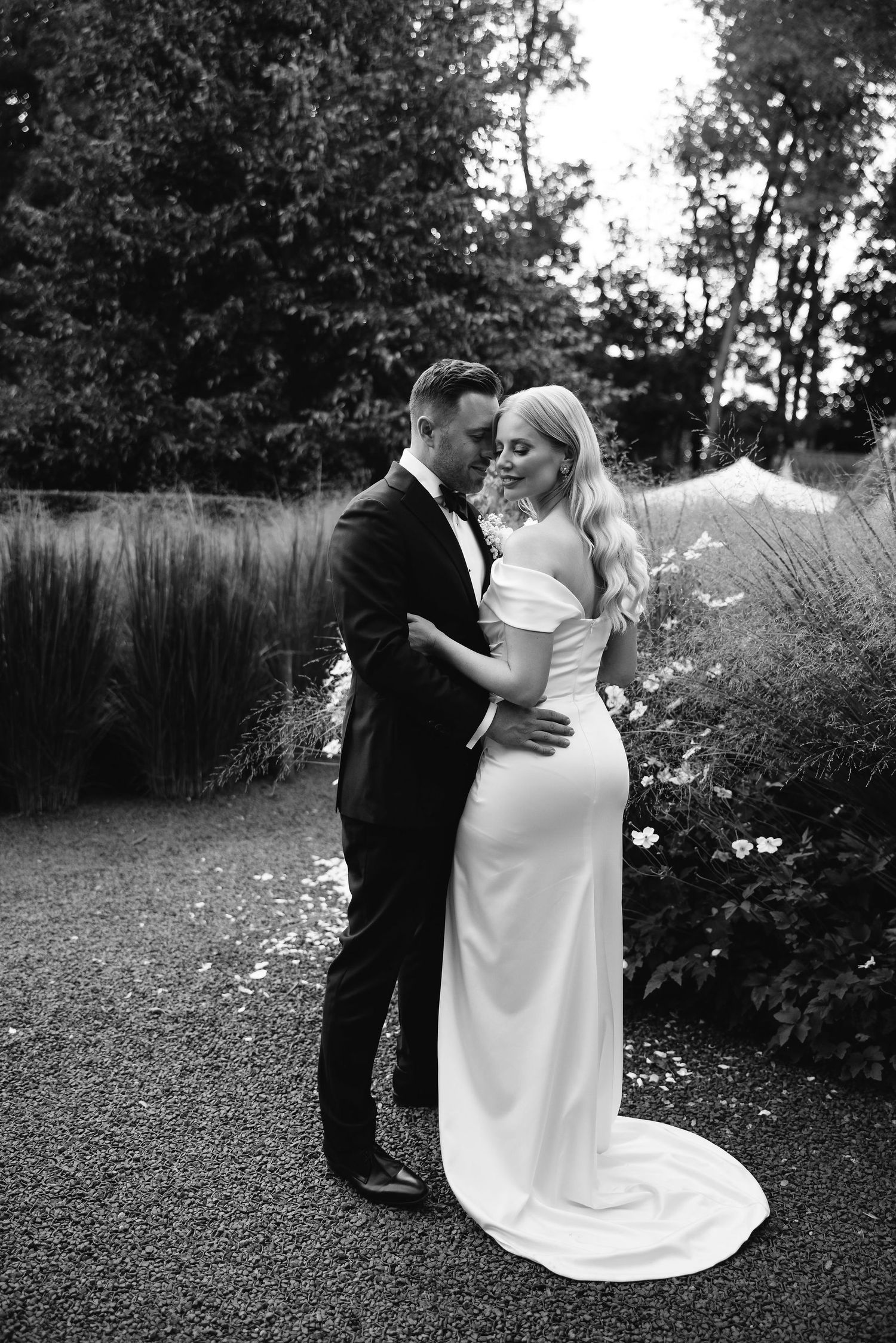 A romantic outdoor wedding scene with a couple dancing together in formal attire among garden greenery.