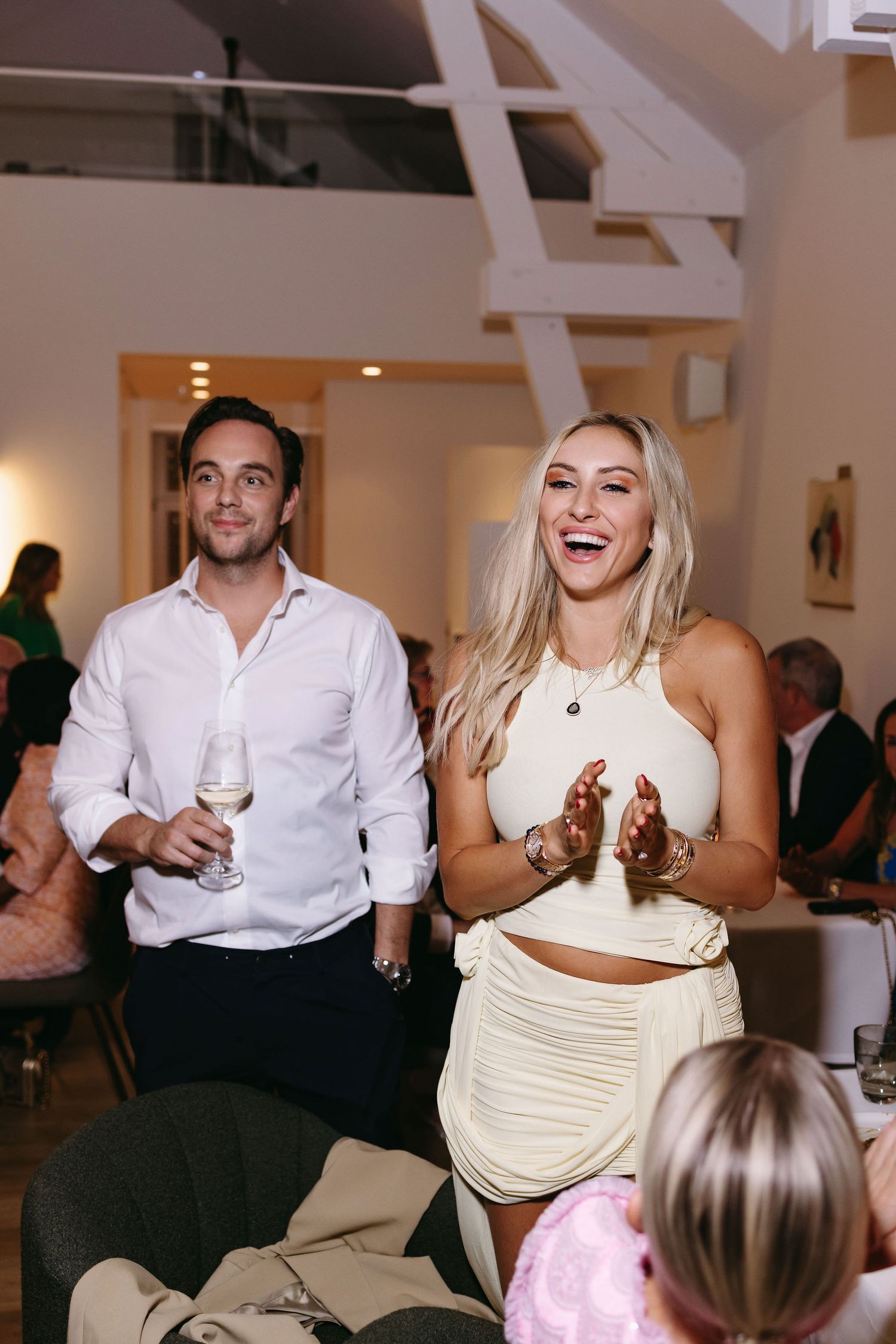 Wedding celebration with guests in white and cream attire enjoying drinks and laughter at a reception.