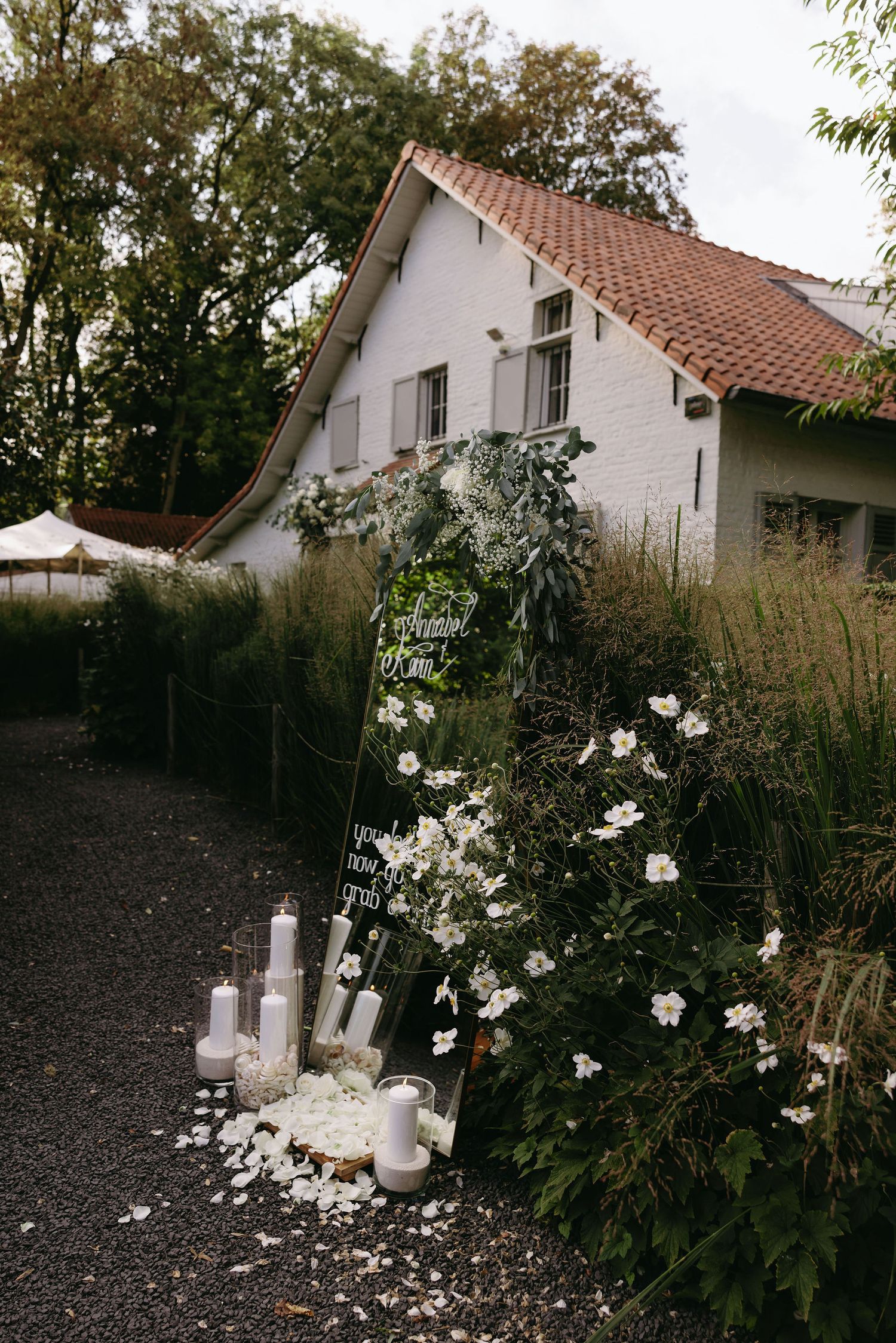 White house with pitched roof surrounded by garden flowers and lit candles.