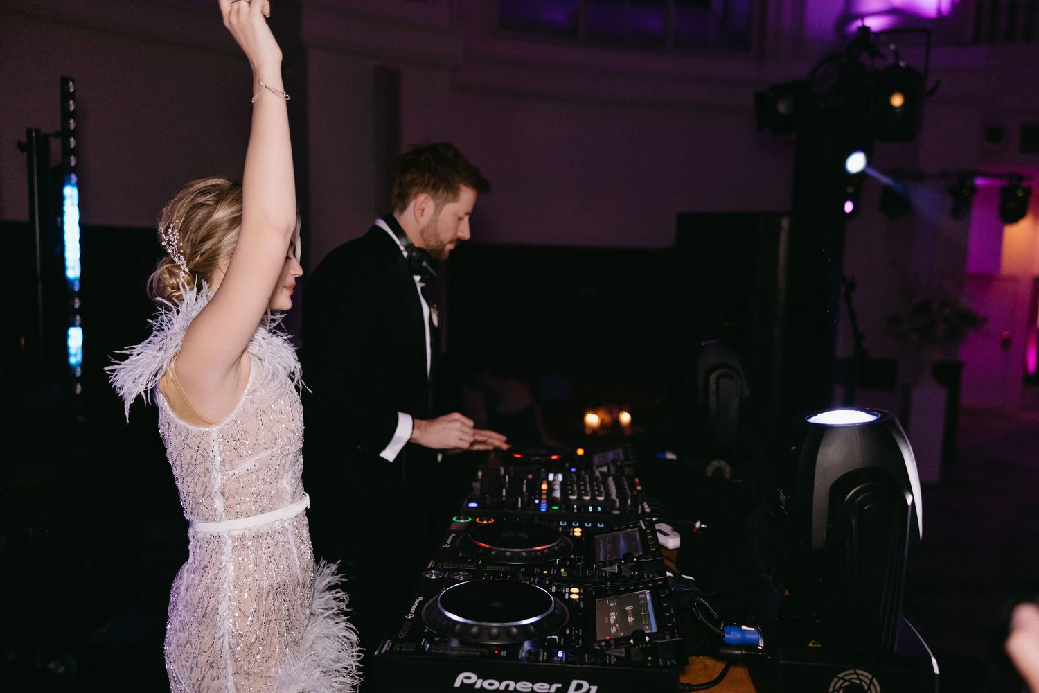 Wedding celebration at DJ booth with feather-trimmed dress and dance party lighting.