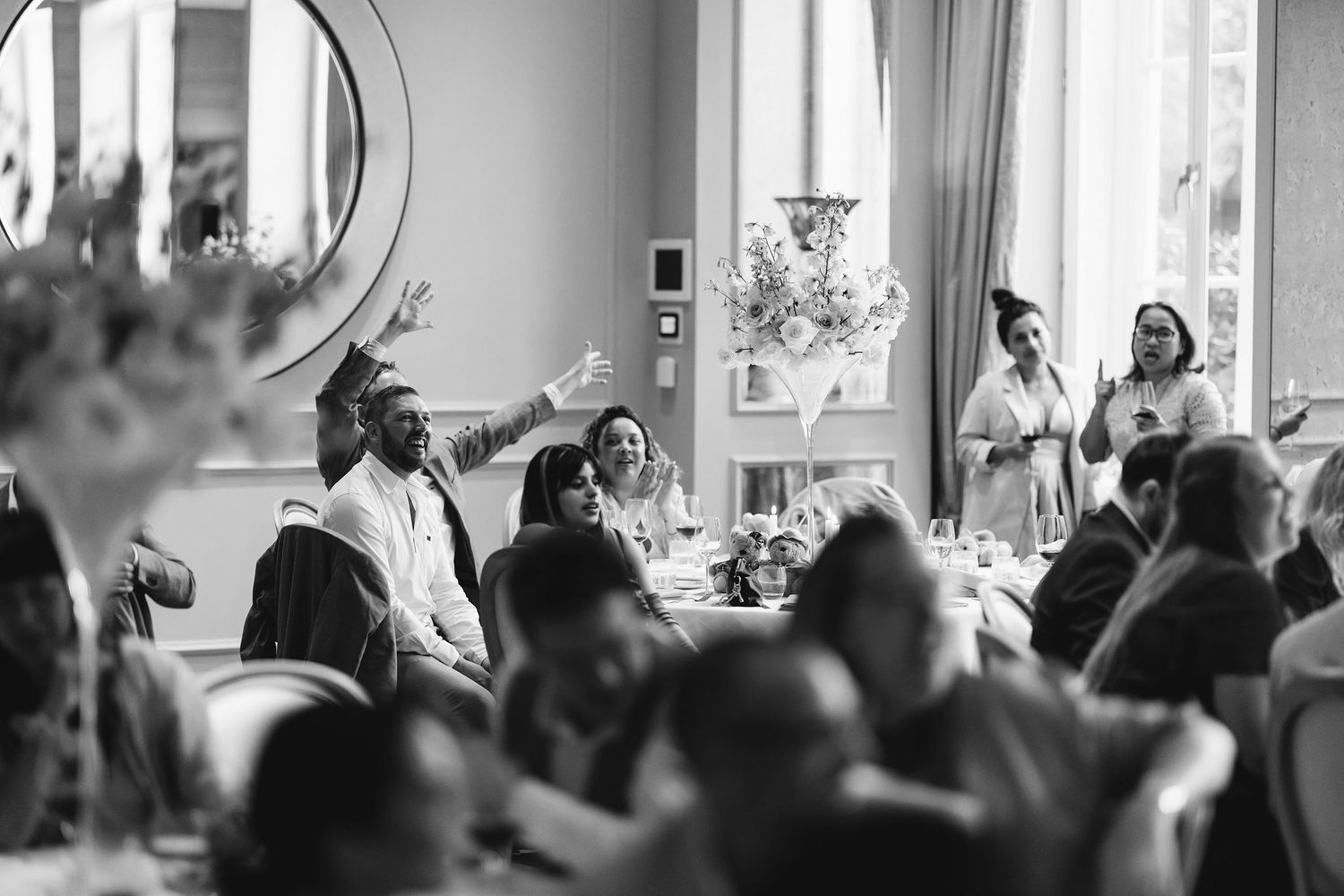 A black and white photo of wedding guests enjoying speeches during the reception.