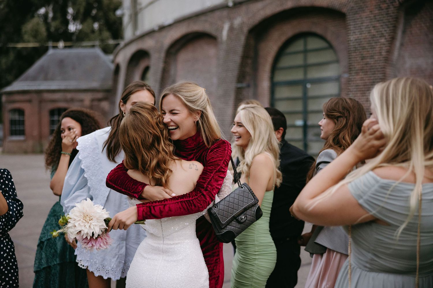 Wedding party poses together outside a brick building during outdoor festivities.