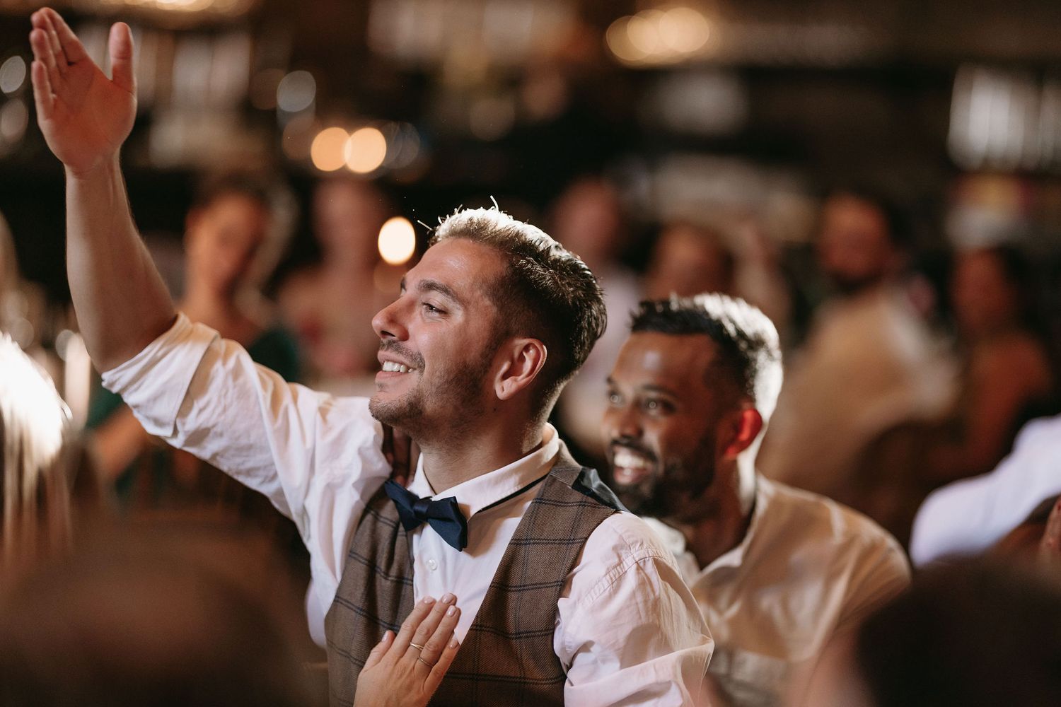 Wedding guests dancing and celebrating on a dimly lit dance floor.