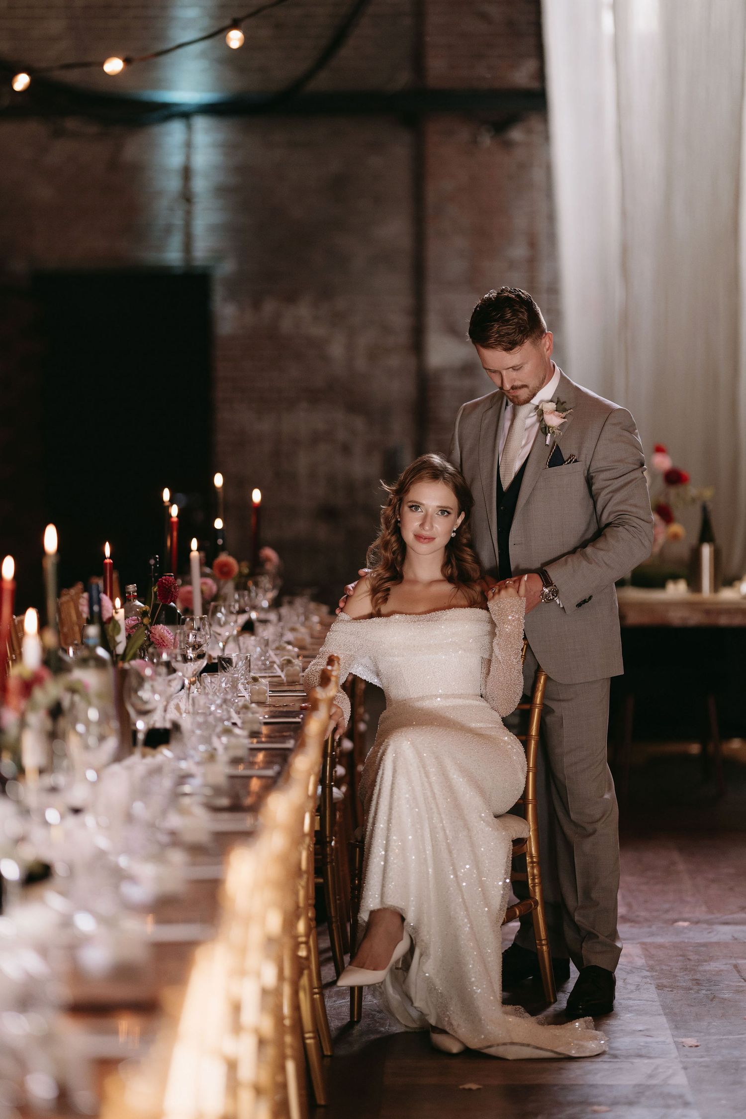 Elegant wedding reception table setting with candles and formal place settings in industrial venue.