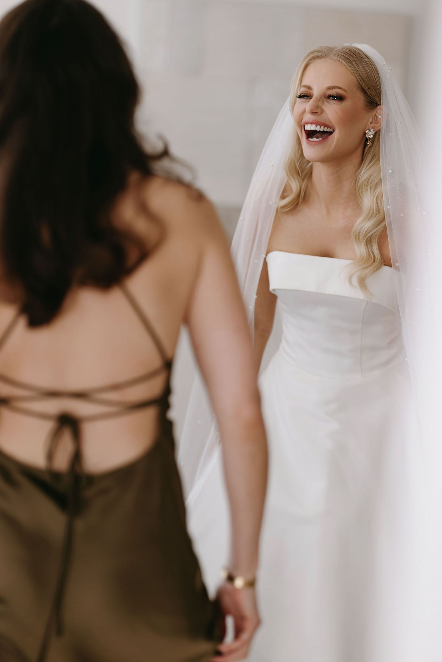 Elegant bride in strapless white gown laughing with joy.