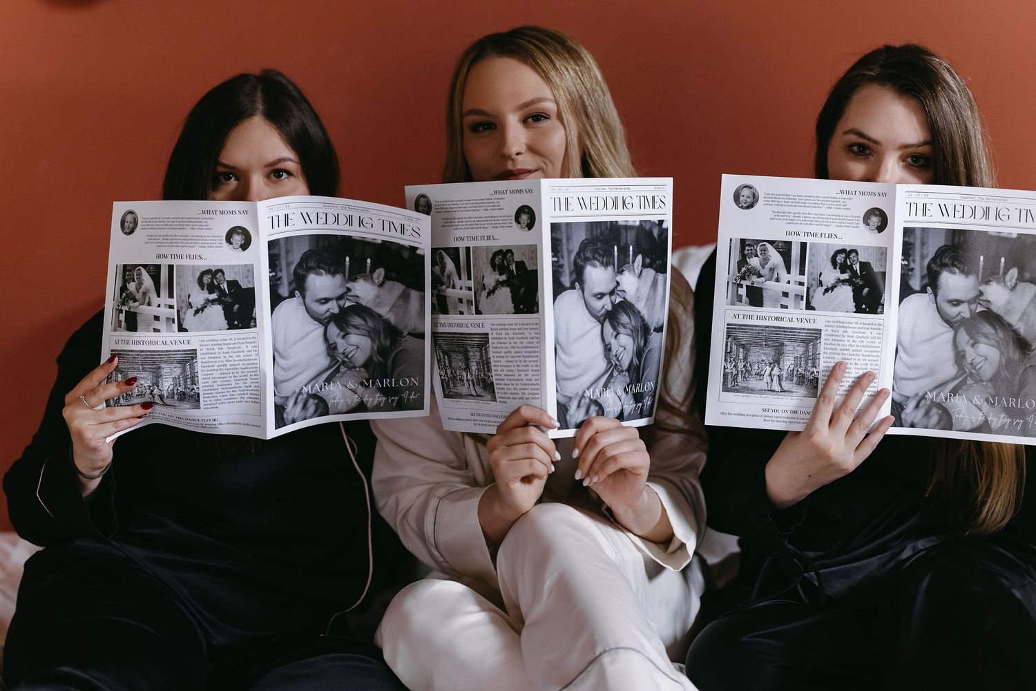 Three friends holding up matching photo books while sitting on couch.