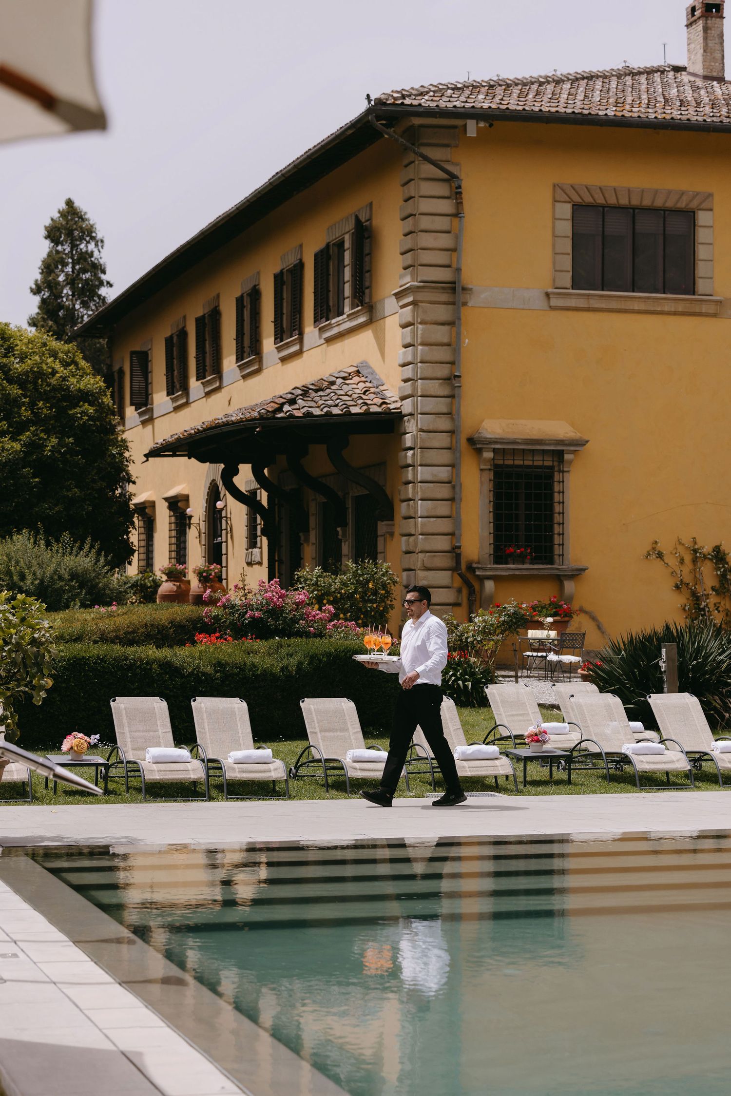 Elegant yellow Italian villa with pool loungers and manicured gardens in Tuscany.