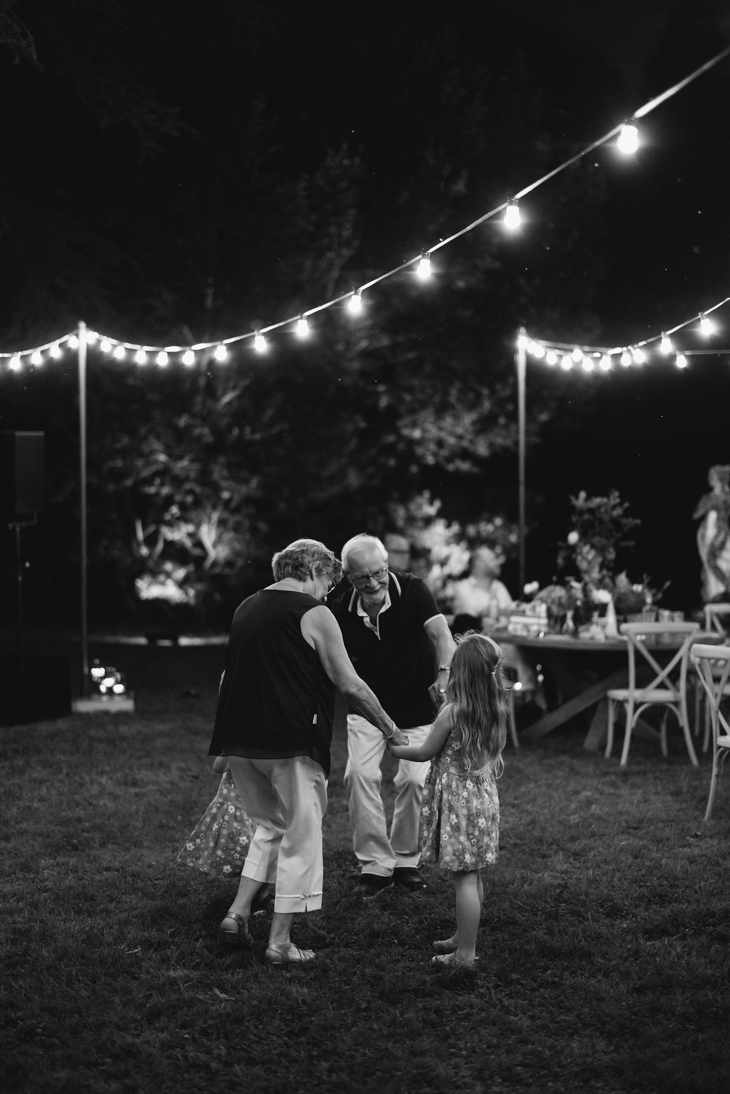 People dancing outdoors at night under romantic string lights in a garden setting.