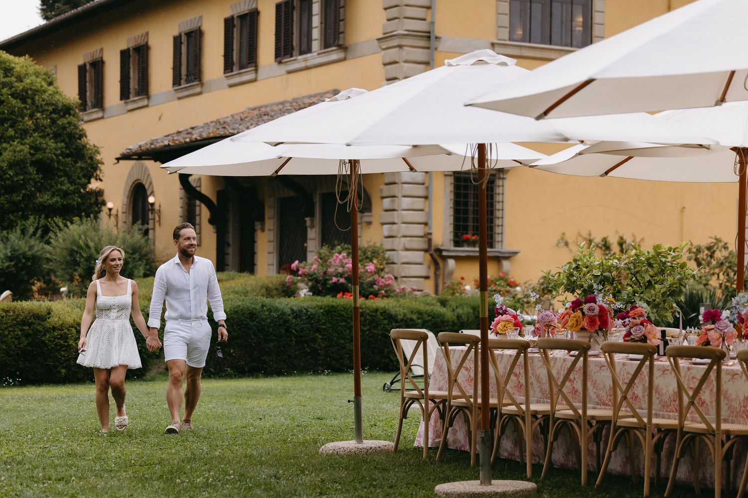 Elegant outdoor wedding setup with white umbrellas and rustic wooden tables at an Italian villa.