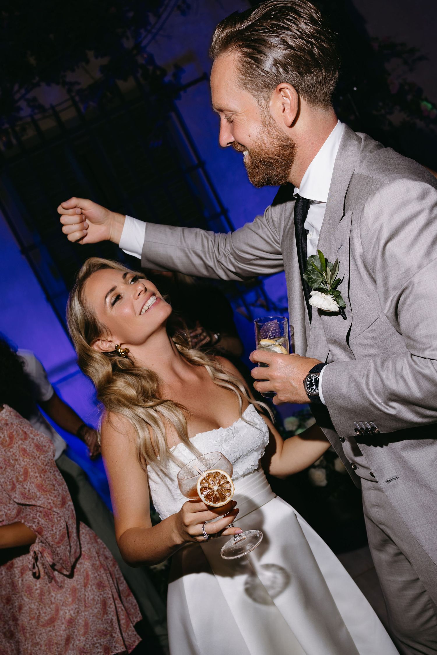Lively wedding reception celebration with dancing and champagne under blue lighting.