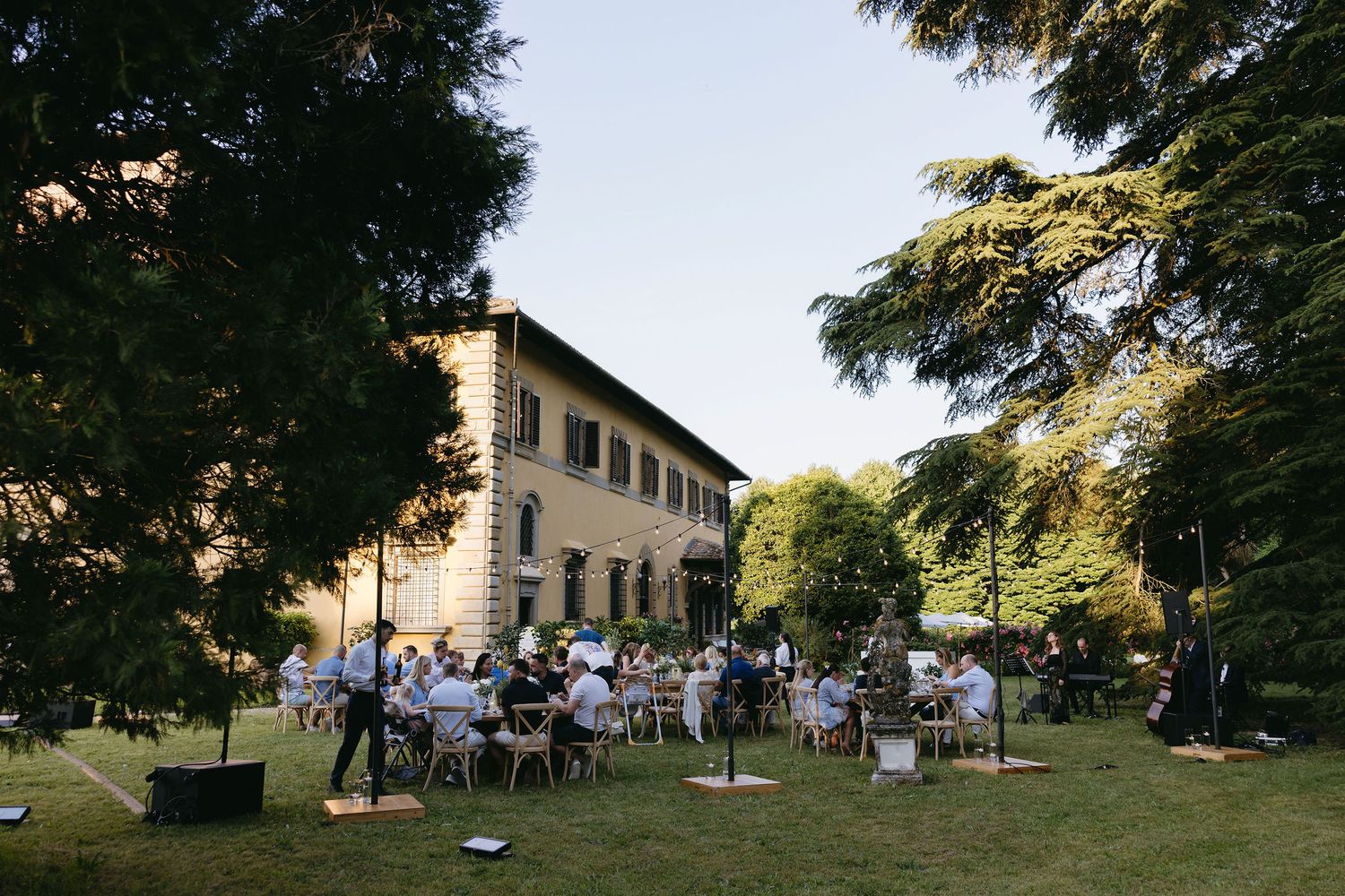 Scenic outdoor wedding venue with elegant villa and lush garden setting at sunset.