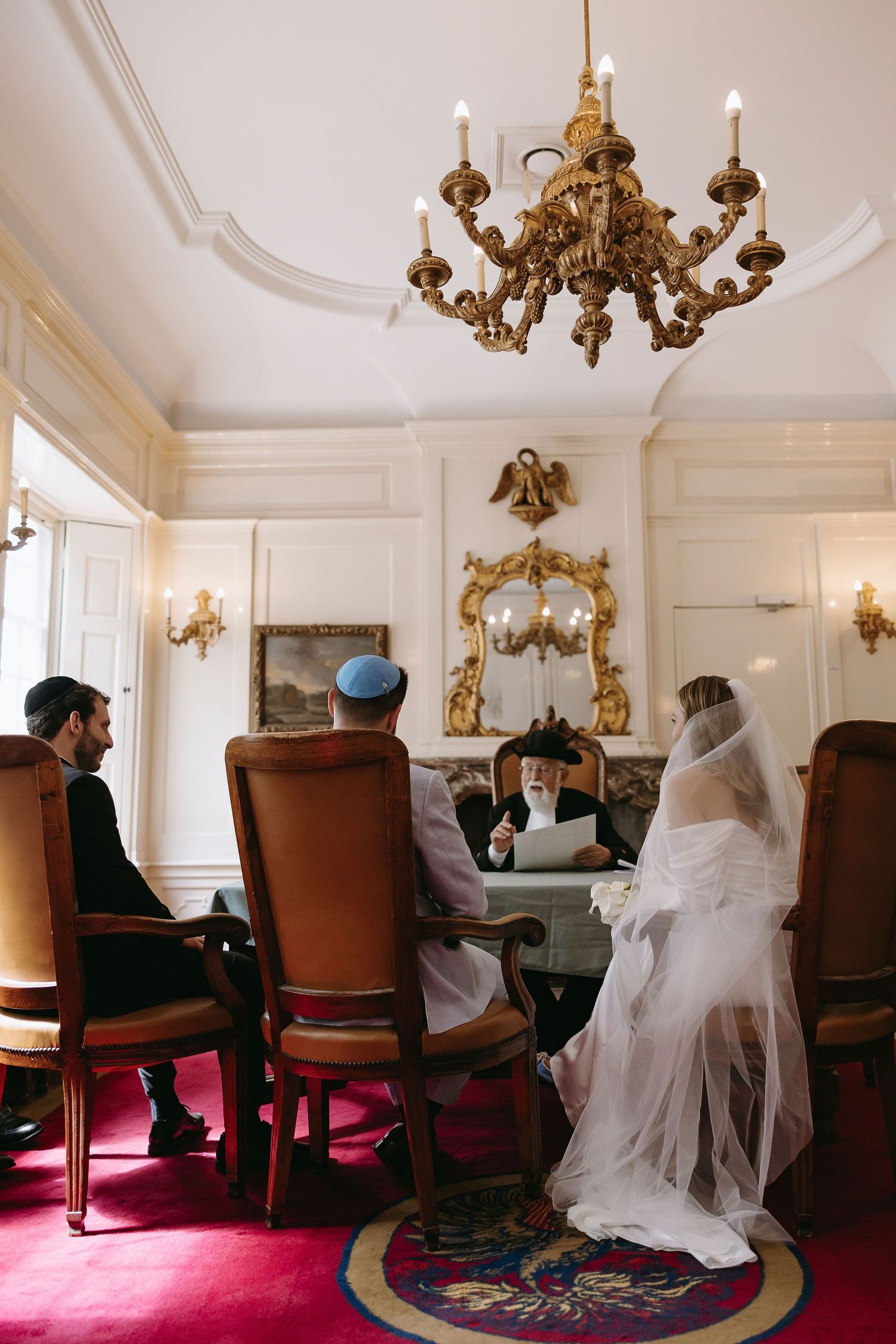 Elegant room with ornate chandeliers and red chairs during wedding ceremony.