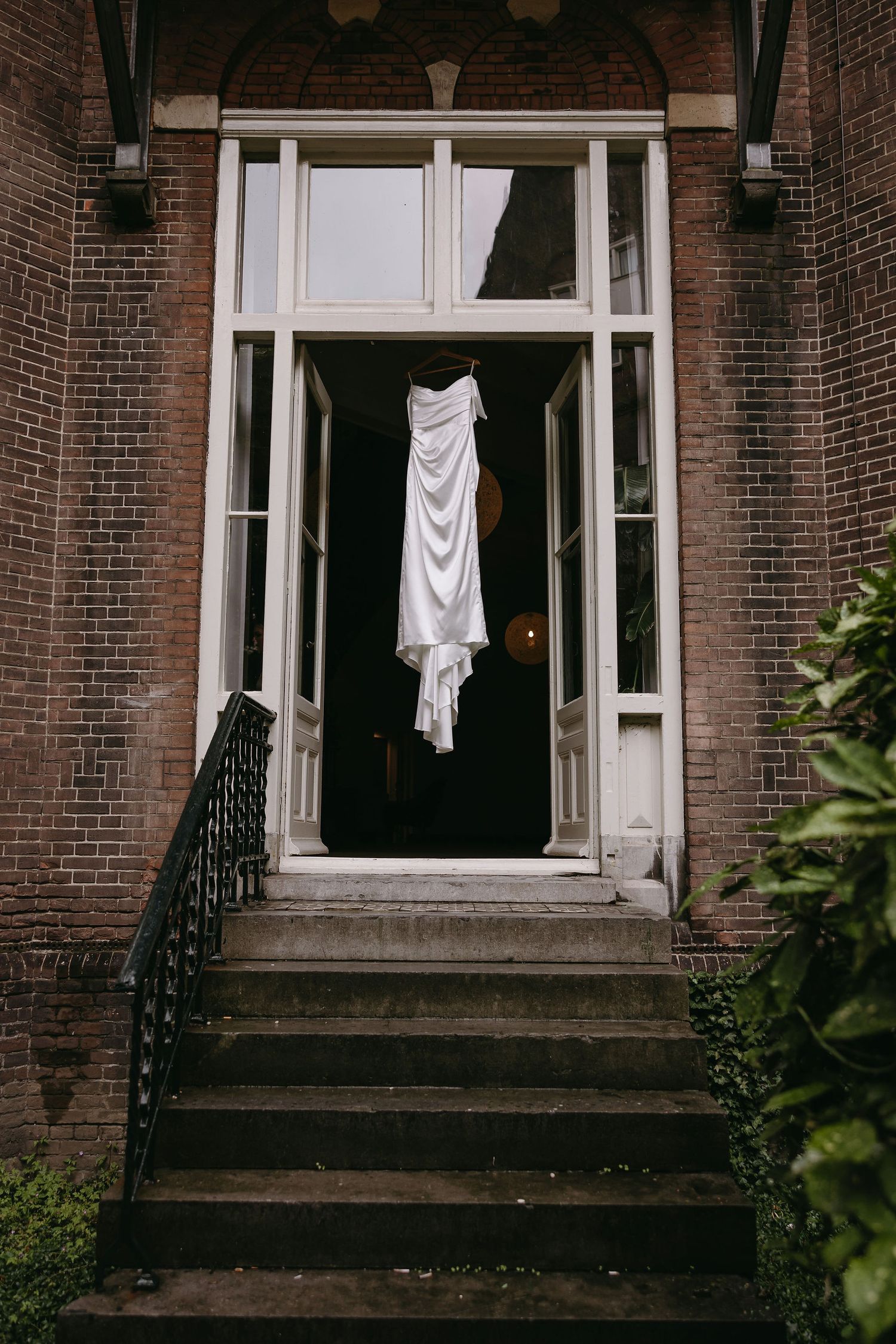 White wedding dress hanging in dark doorframe of brick building entrance.