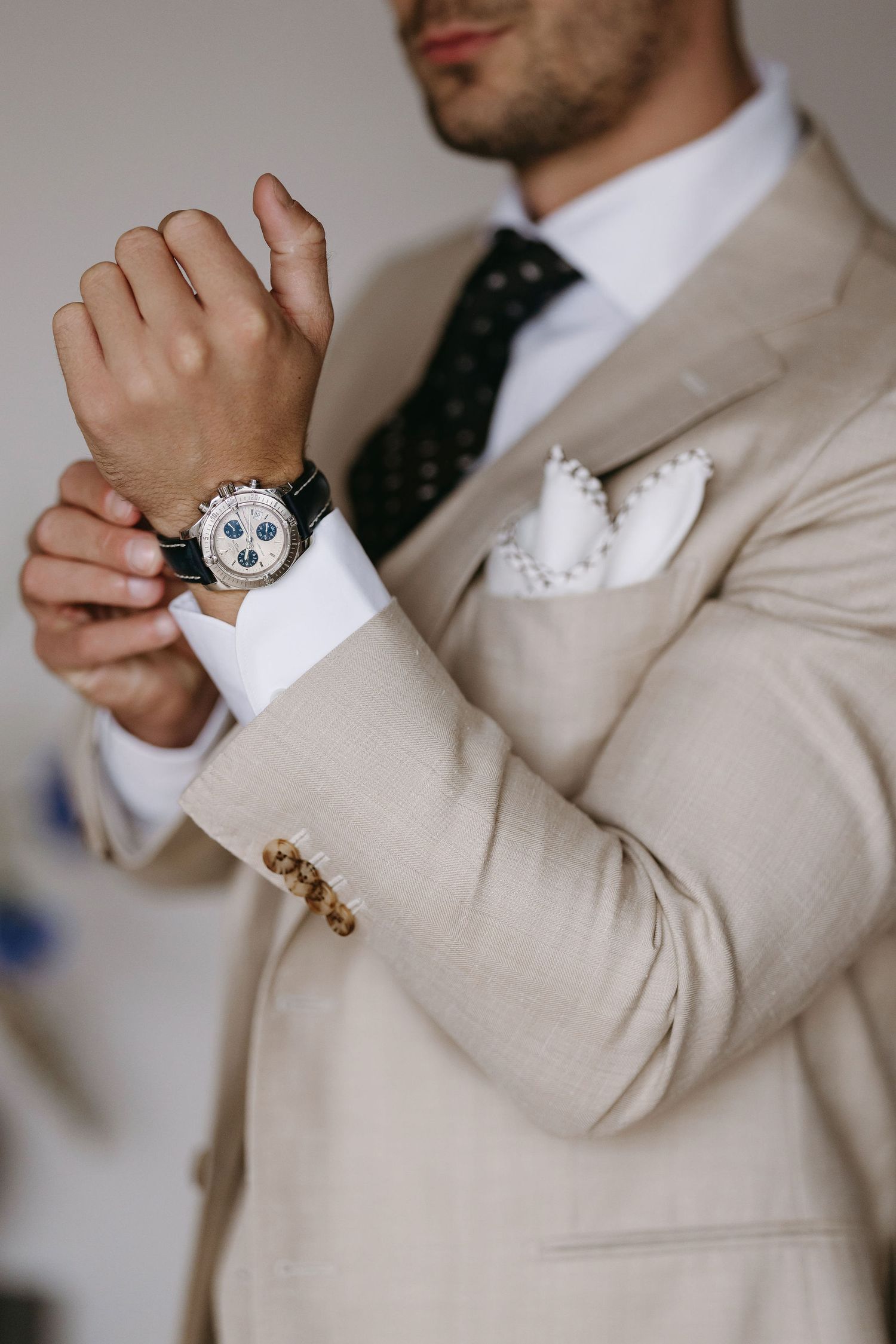 Close-up details of a beige suit with cufflinks and polka dot tie.
