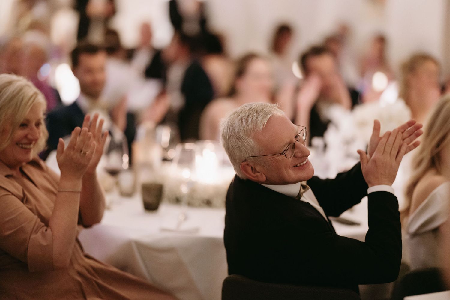Reception guests enthusiastically applauding during wedding celebration dinner.