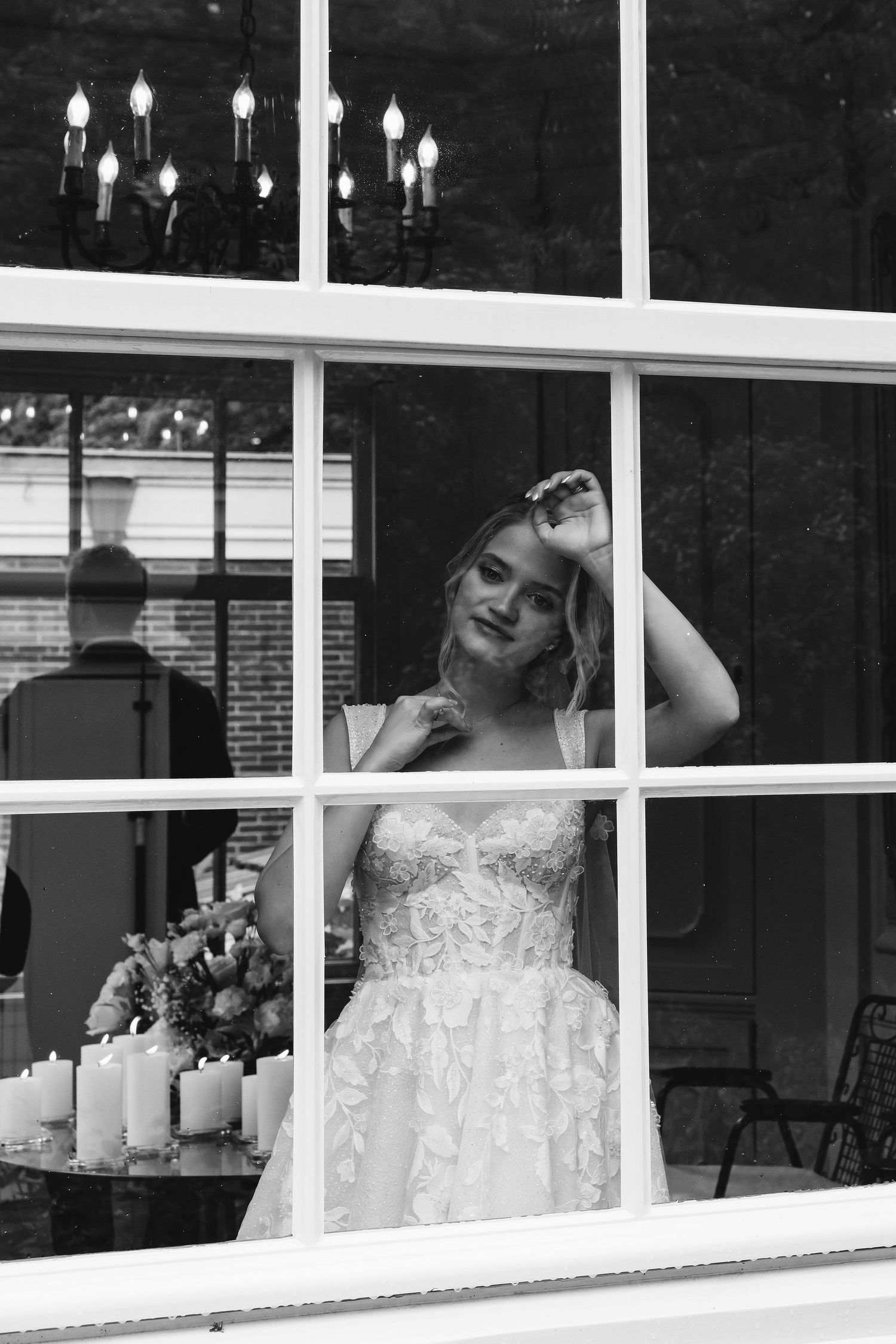 Wedding dress displayed through window panes with soft lighting and candles.