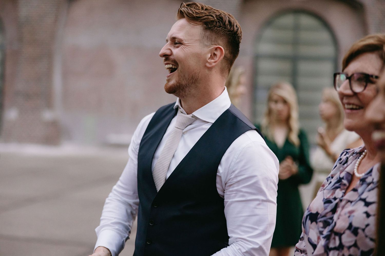 A joyful moment captured during an outdoor wedding reception with guests mingling in formal attire.