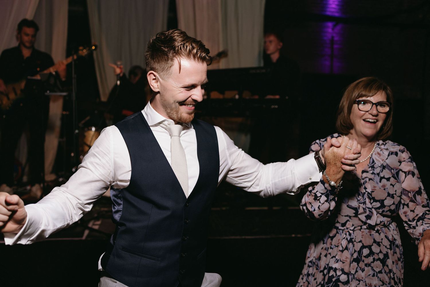 Reception guests dancing and celebrating under purple venue lighting.