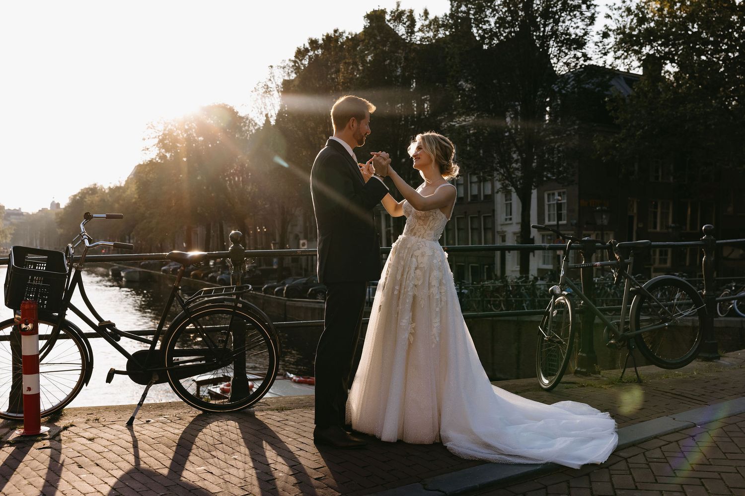 Couple celebrates their wedding day outdoors with bikes visible in silhouette during golden hour sunset.