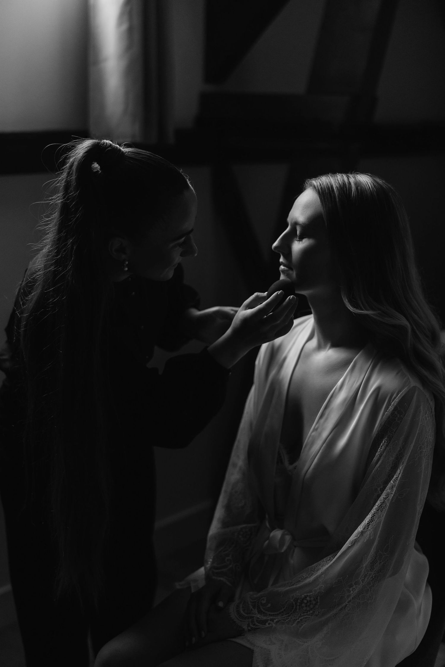 Atmospheric black and white photo of wedding day makeup application in moody lighting.