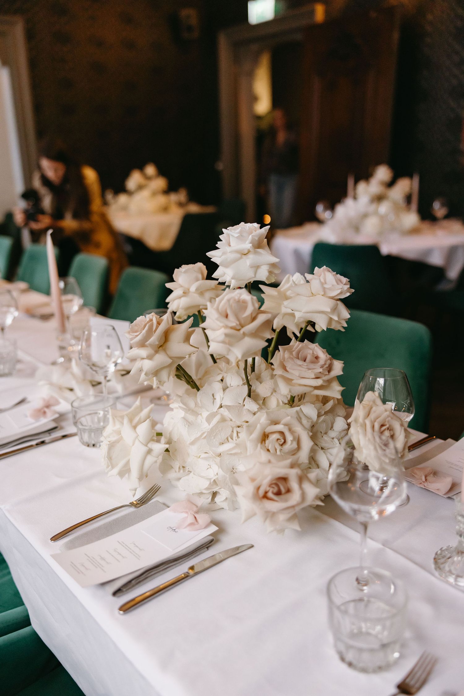 Elegant wedding table setting with white roses and place settings on crisp white tablecloth.