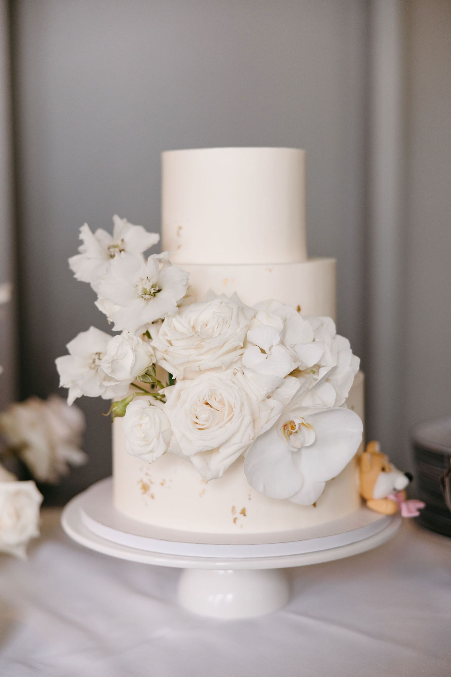 A simple white wedding cake decorated with elegant fresh white flowers on top.