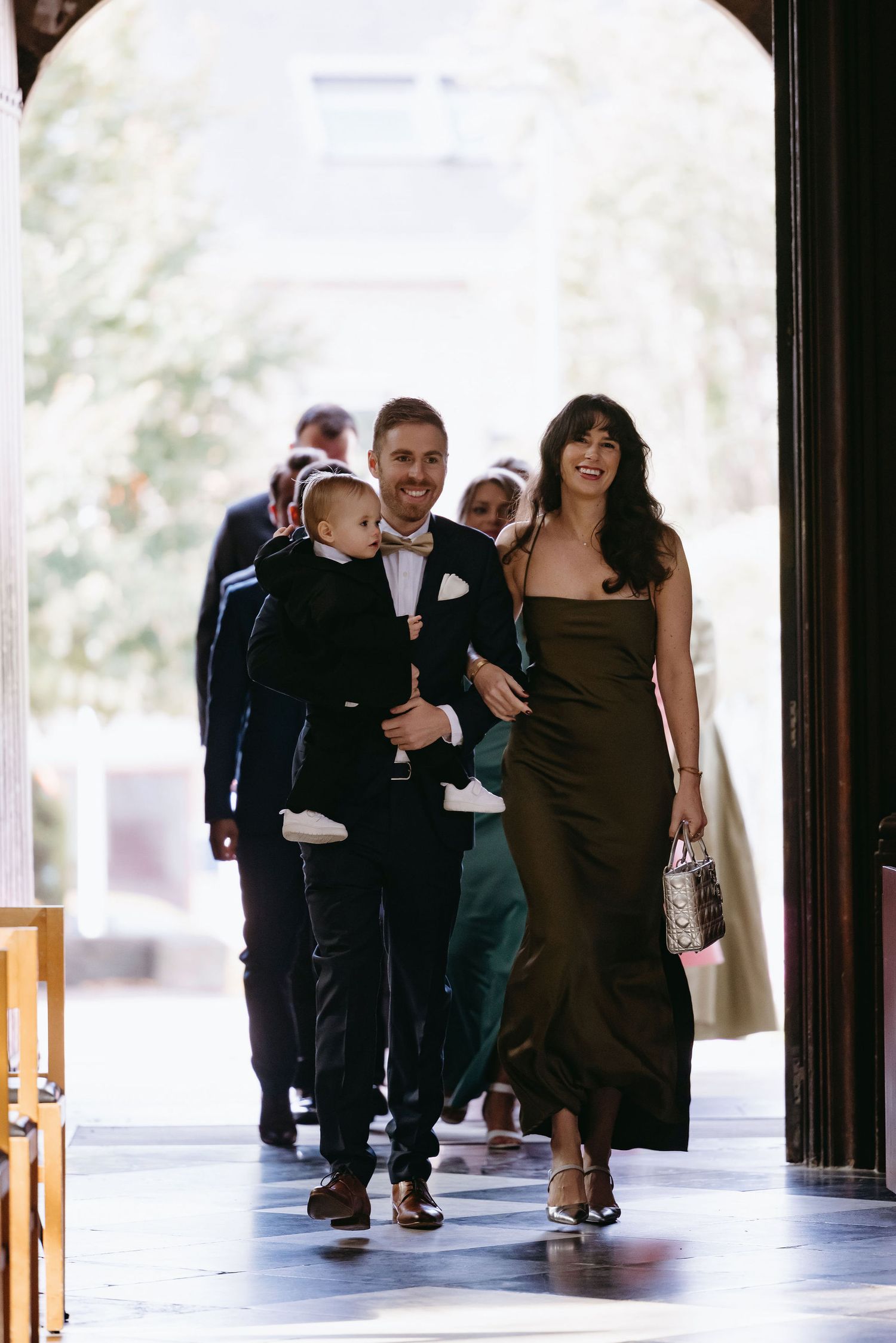 Wedding guests walk down a covered walkway in formal attire during a joyous celebration.