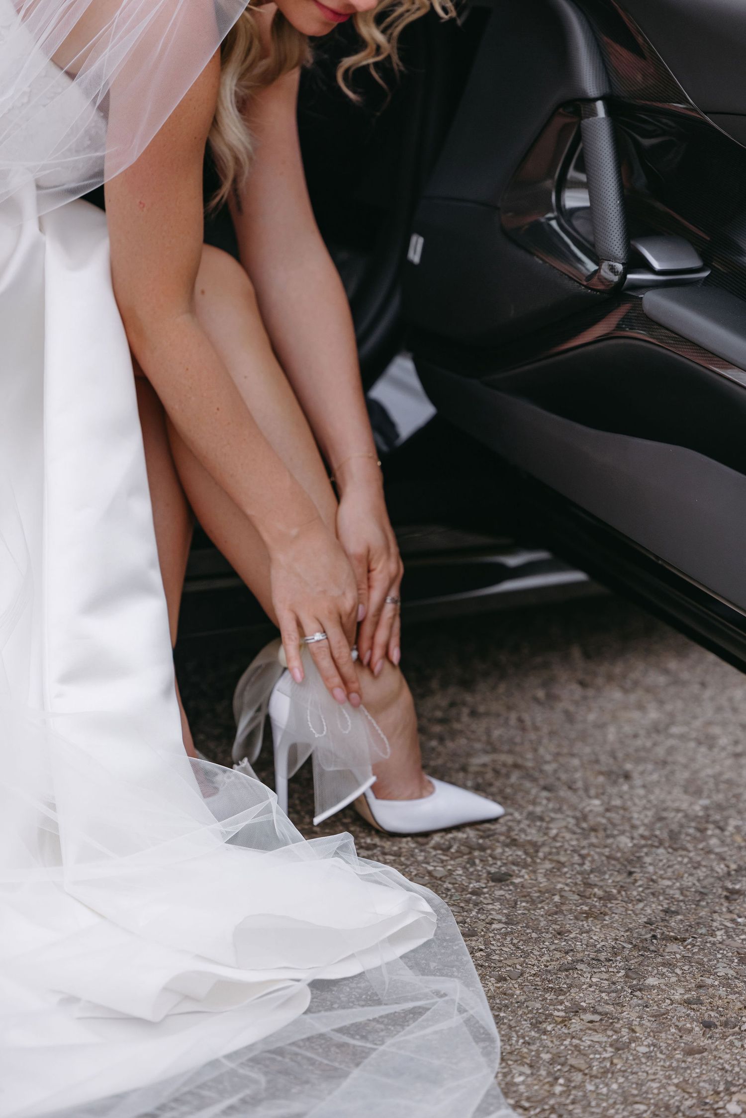 White wedding shoes and flowing veil detail in a car.